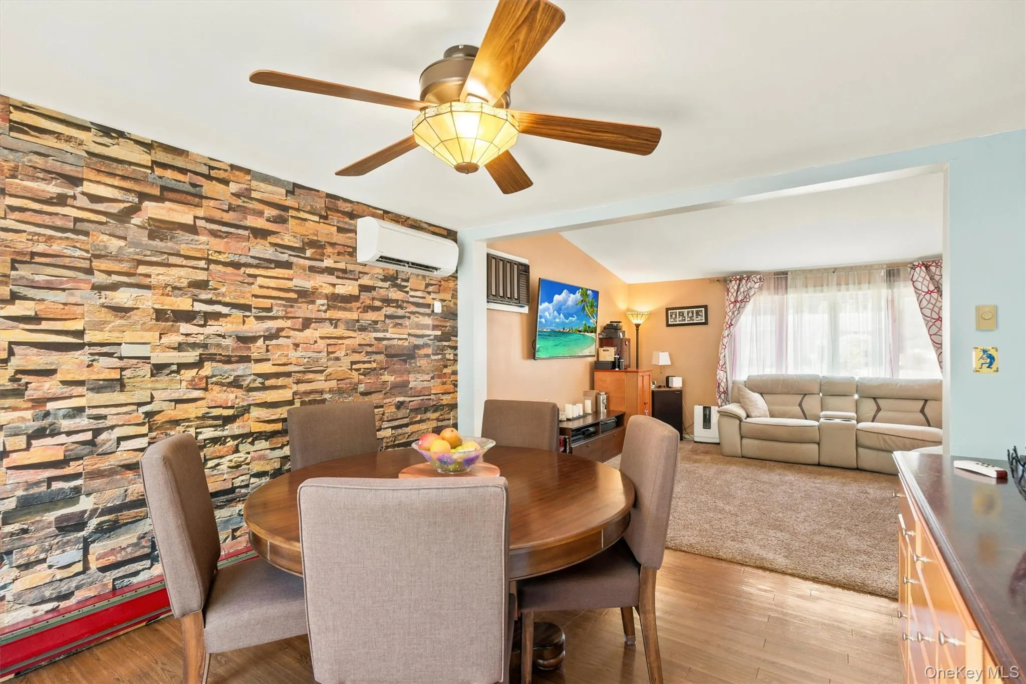 Dining area featuring a stone-look accent wall, wood-finish flooring, and a ceiling fan with integrated lighting Dining area featuring a stone-look accent wall, wood-finish flooring, and a ceiling fan with integrated lighting
