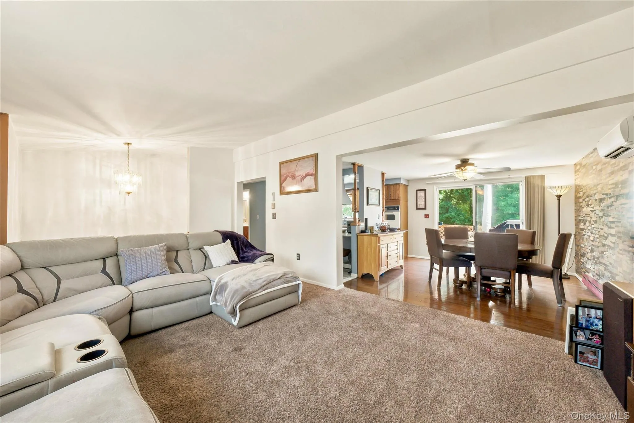 Open-concept living area featuring soft brown carpeting, a formal dining space with wood-finish flooring, and a decorative chandelier Open-concept living area featuring soft brown carpeting, a formal dining space with wood-finish flooring, and a decorative chandelier