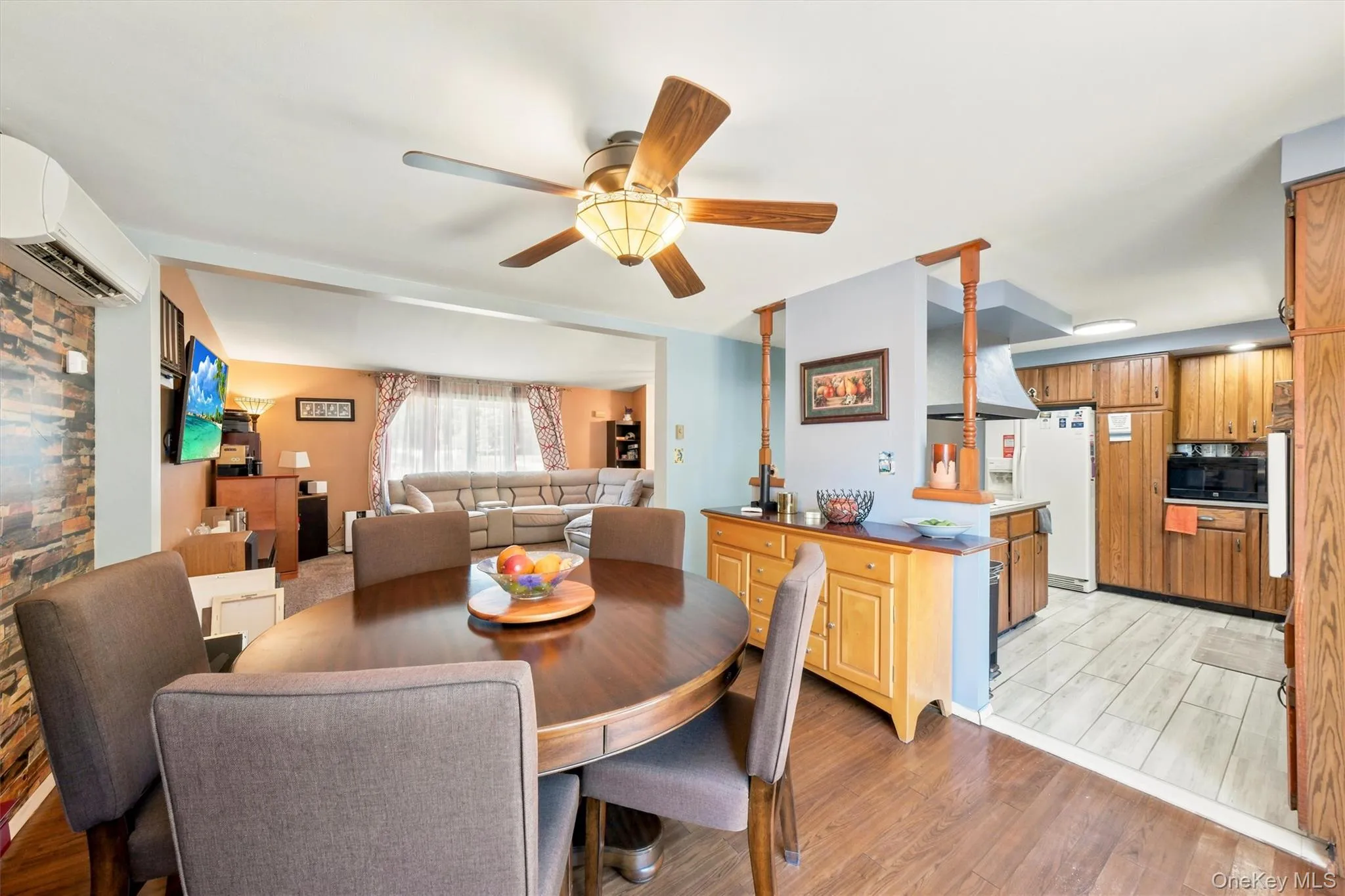 Open-concept dining area featuring wood-finish flooring, a ceiling fan with integrated lighting, and a built-in air conditioning unit Open-concept dining area featuring wood-finish flooring, a ceiling fan with integrated lighting, and a built-in air conditioning unit