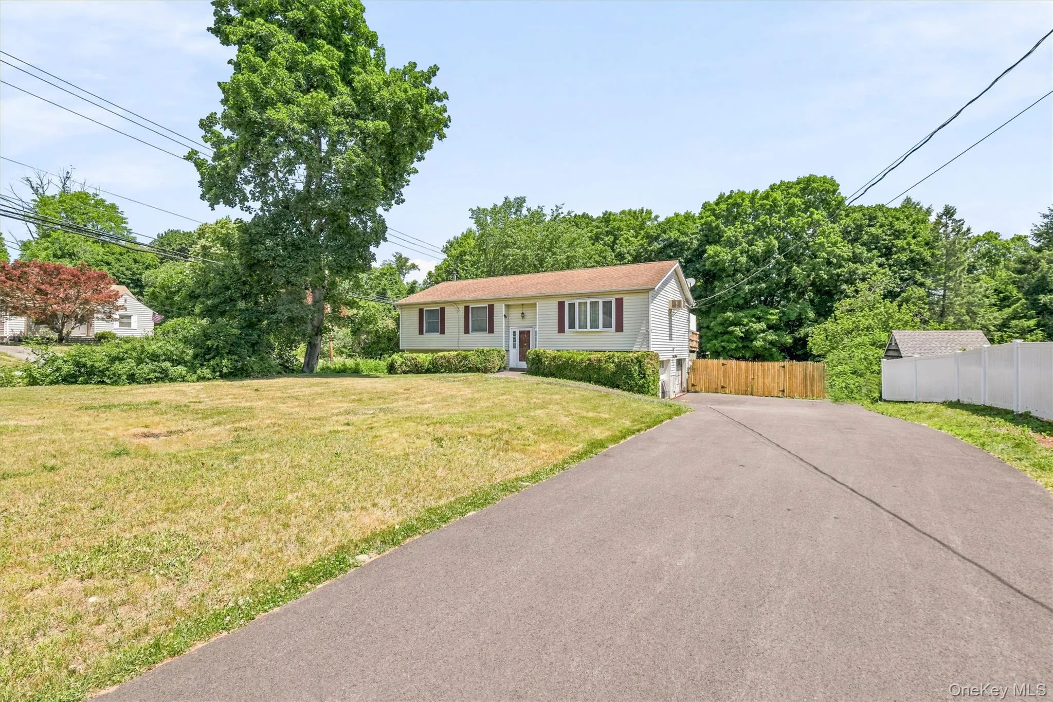 Raised Ranch-style residence featuring a light-colored exterior with red shutters, a paved driveway, and a large front lawn Raised Ranch-style residence featuring a light-colored exterior with red shutters, a paved driveway, and a large front lawn