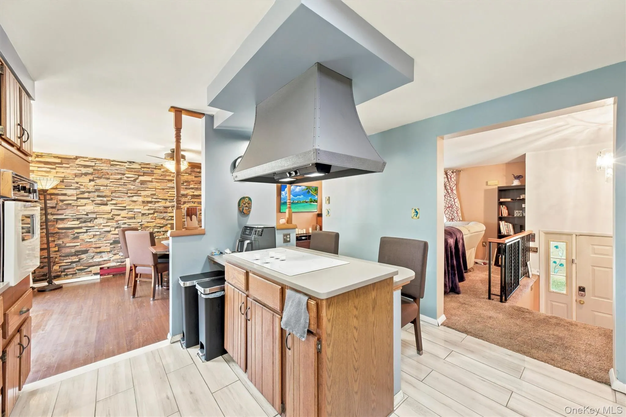 Kitchen island featuring a built-in cooktop, light-colored countertop, and a contemporary range hood Kitchen island featuring a built-in cooktop, light-colored countertop, and a contemporary range hood