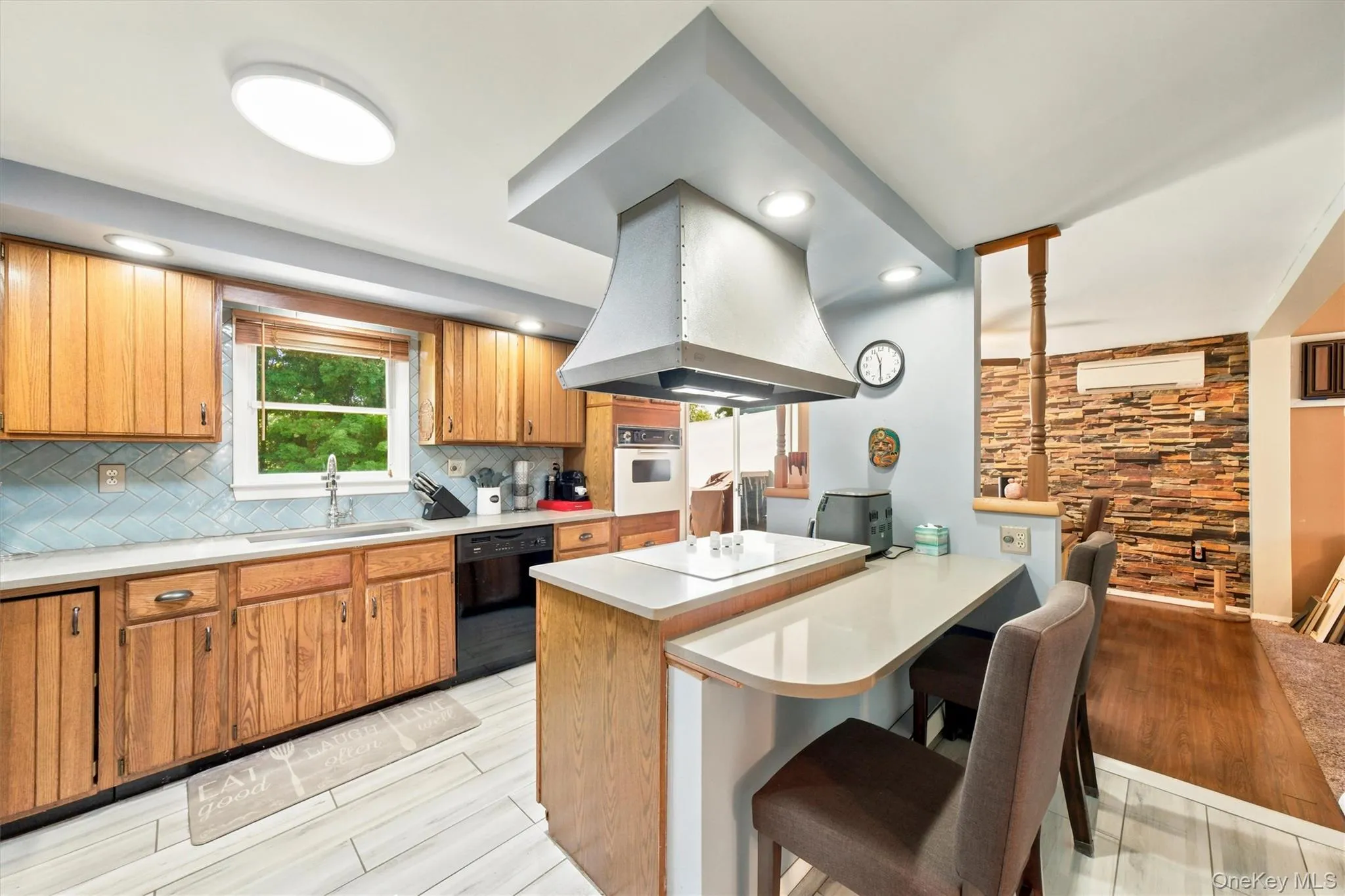 Kitchen featuring light wood cabinetry, blue herringbone tile backsplash, and a built-in cooktop with a stainless steel range hood Kitchen featuring light wood cabinetry, blue herringbone tile backsplash, and a built-in cooktop with a stainless steel range hood