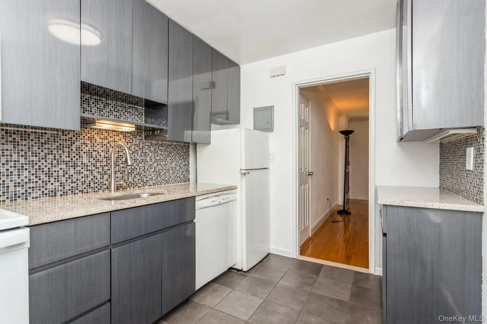 Kitchen with gray cabinets, white appliances, backsplash, light stone counters, and dark tile patterned flooring Kitchen with gray cabinets, white appliances, backsplash, light stone counters, and dark tile patterned flooring