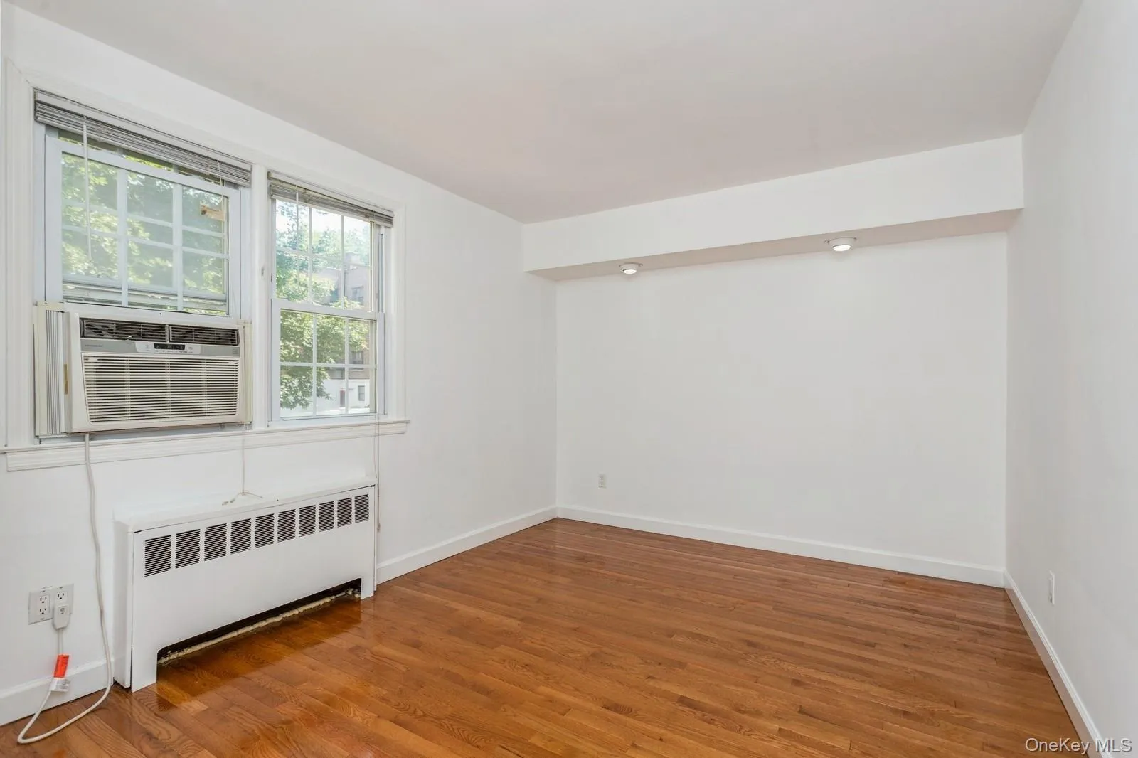 Unfurnished room featuring radiator, wood finished floors, and cooling unit Unfurnished room featuring radiator, wood finished floors, and cooling unit