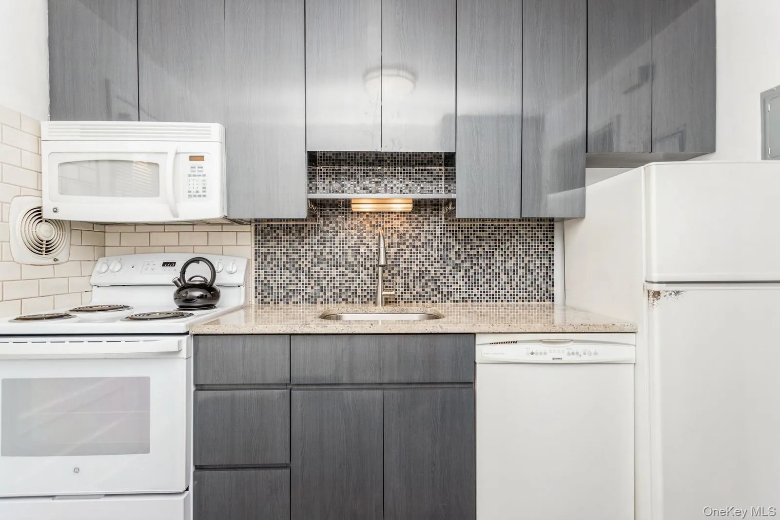 Kitchen featuring white appliances, gray cabinetry, decorative backsplash, and light stone counters Kitchen featuring white appliances, gray cabinetry, decorative backsplash, and light stone counters