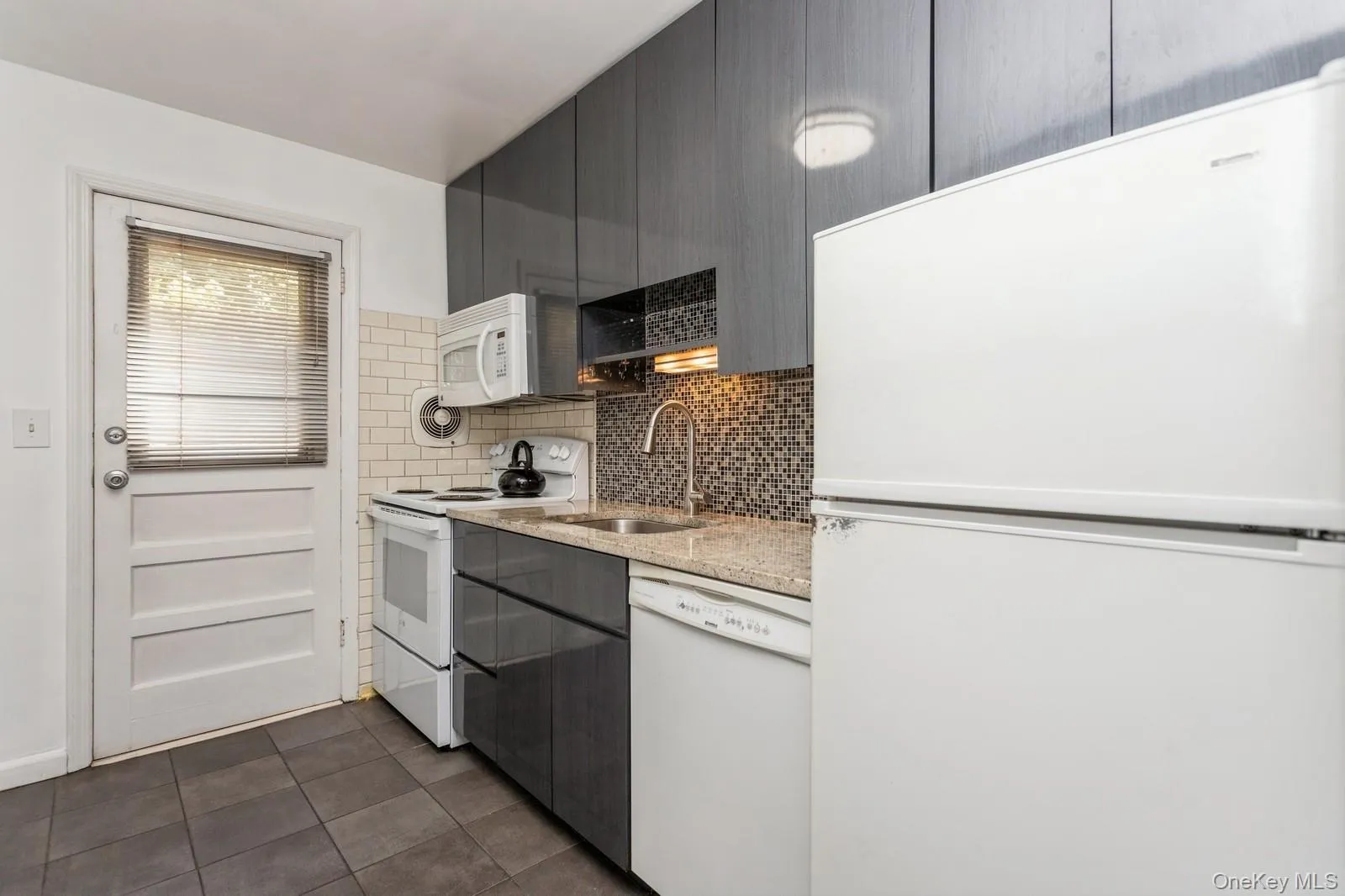 Kitchen with white appliances, dark tile patterned flooring, backsplash, light stone countertops, and modern cabinets Kitchen with white appliances, dark tile patterned flooring, backsplash, light stone countertops, and modern cabinets