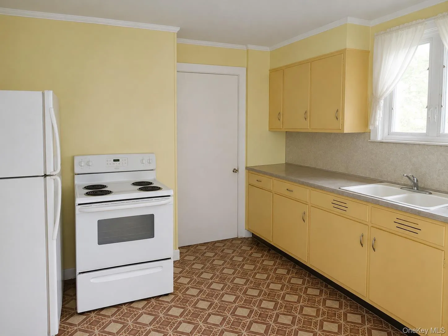 Kitchen featuring yellow cabinetry, white double-basin sink, light-toned countertop, and patterned floor tiling Kitchen featuring yellow cabinetry, white double-basin sink, light-toned countertop, and patterned floor tiling