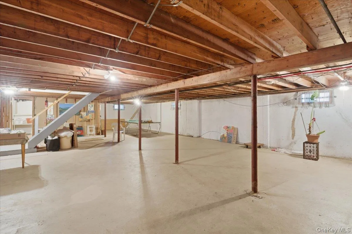 Spacious unfinished basement featuring exposed wood joists, structural support columns, concrete flooring, and perimeter lighting Spacious unfinished basement featuring exposed wood joists, structural support columns, concrete flooring, and perimeter lighting