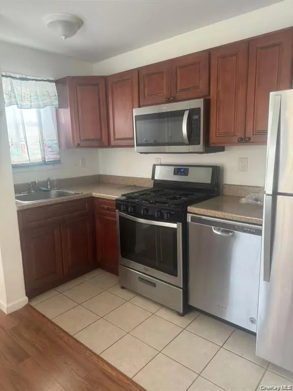 Well-appointed kitchen featuring wood cabinetry, stainless steel appliances, and a tiled floor Well-appointed kitchen featuring wood cabinetry, stainless steel appliances, and a tiled floor