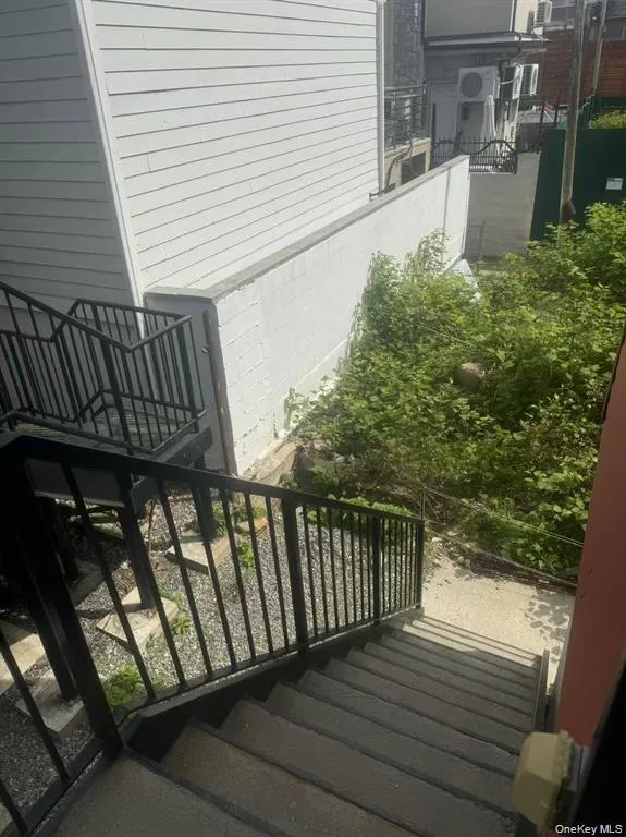 Exterior concrete staircase featuring black metal railings and direct access to a lower-level area with green foliage Exterior concrete staircase featuring black metal railings and direct access to a lower-level area with green foliage