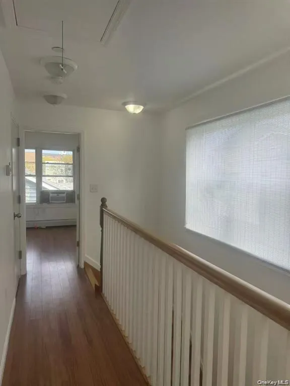 Hallway with wood-finish flooring, a painted white balustrade with a wood handrail, and multiple ceiling-mounted light fixtures Hallway with wood-finish flooring, a painted white balustrade with a wood handrail, and multiple ceiling-mounted light fixtures