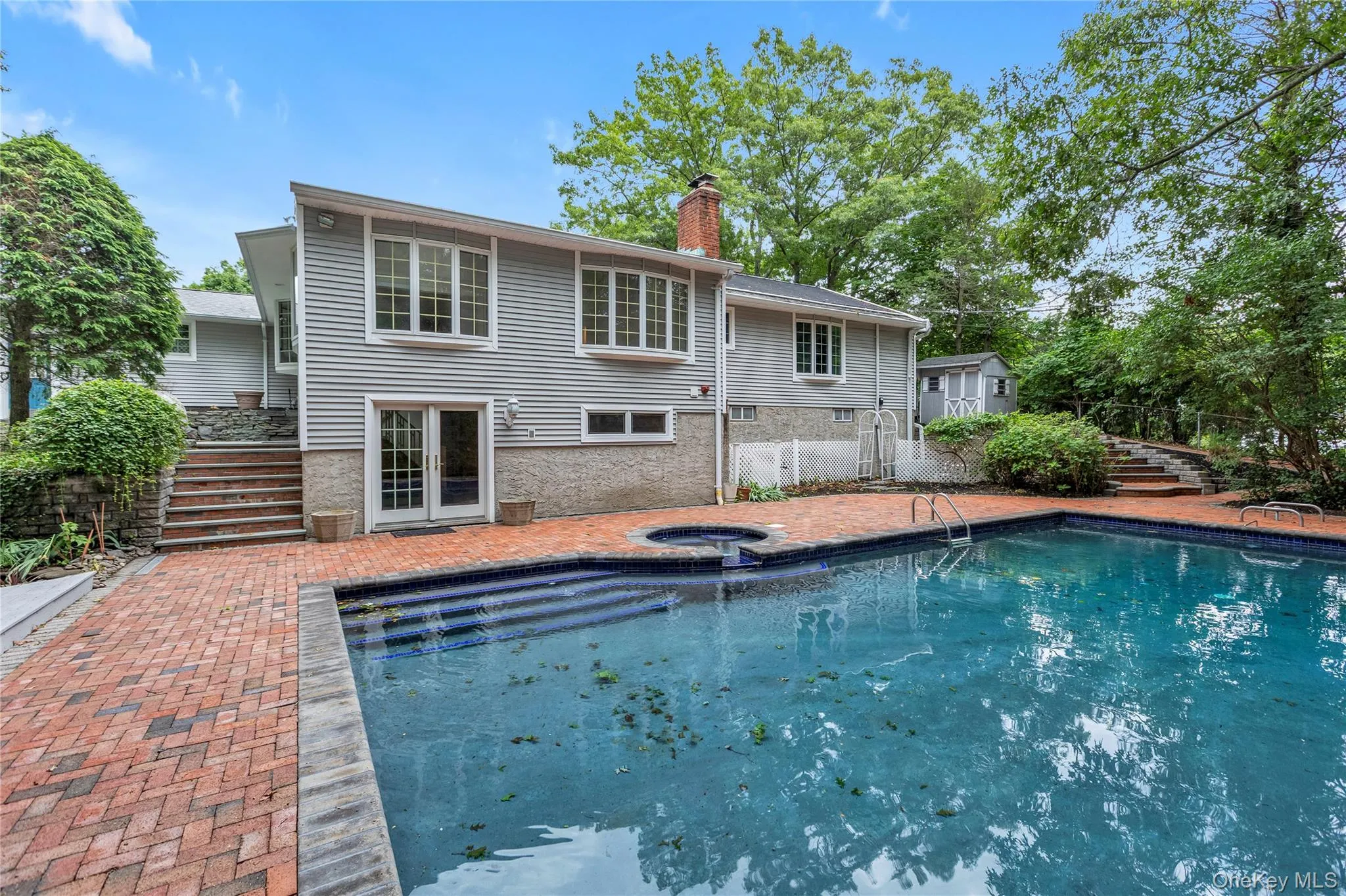 Spacious outdoor area featuring an in-ground swimming pool, adjacent hot tub, and extensive red brick patio Spacious outdoor area featuring an in-ground swimming pool, adjacent hot tub, and extensive red brick patio
