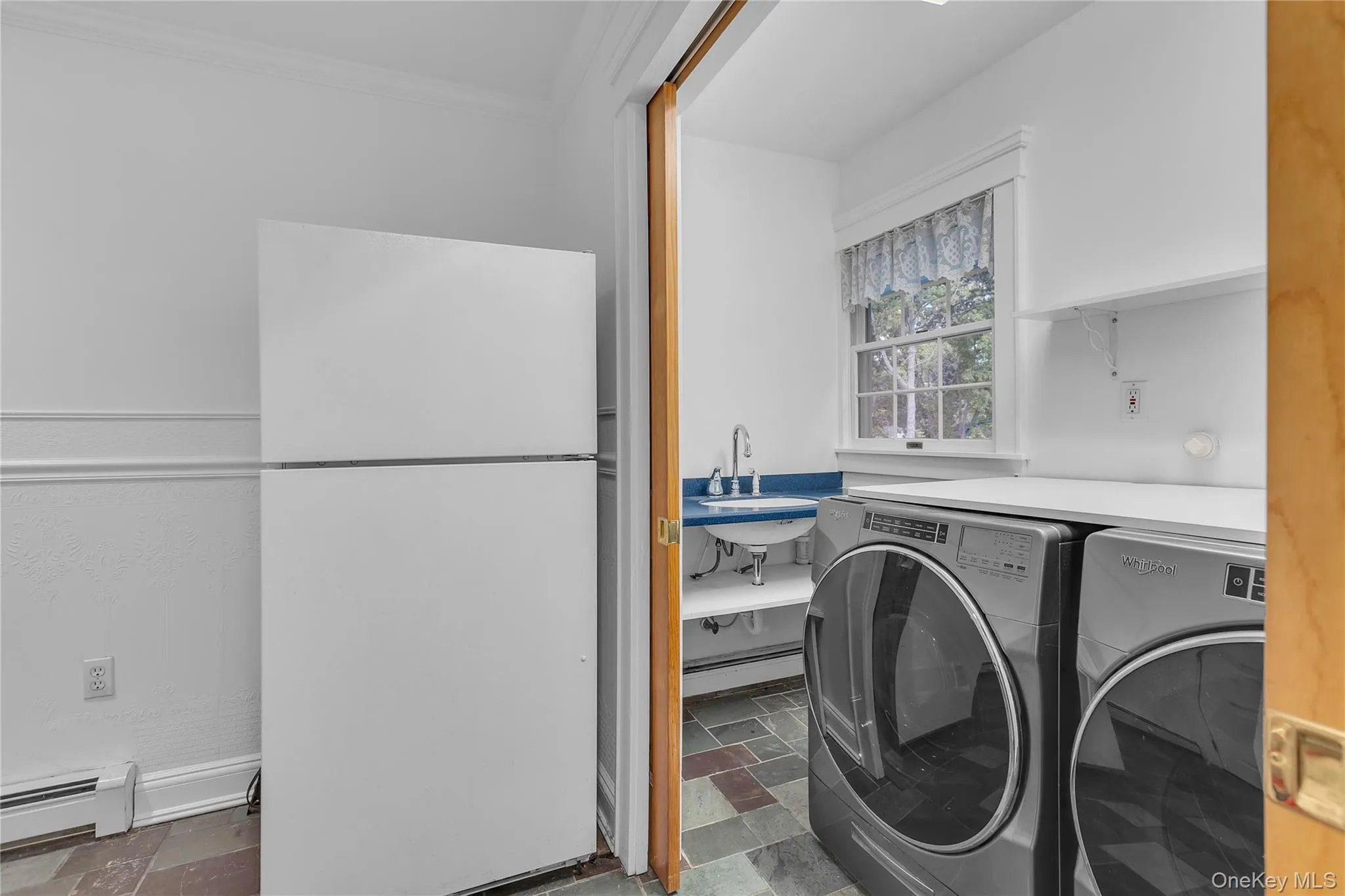 Dedicated laundry area featuring a utility sink with a blue backsplash, slate tile flooring, and a pair of front-loading washer/dryer Dedicated laundry area featuring a utility sink with a blue backsplash, slate tile flooring, and a pair of front-loading washer/dryer