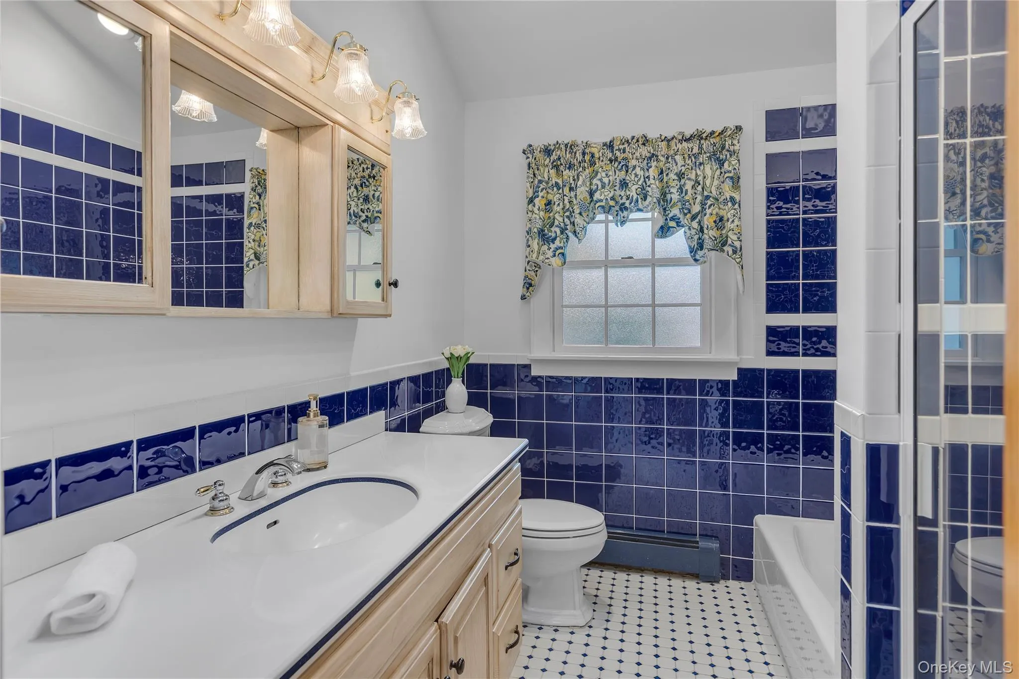 Bathroom with bright blue wall tiling, white vanity with integrated sink, chrome faucet, and mirrored medicine cabinets. Tub and Shower. Bathroom with bright blue wall tiling, white vanity with integrated sink, chrome faucet, and mirrored medicine cabinets. Tub and Shower.