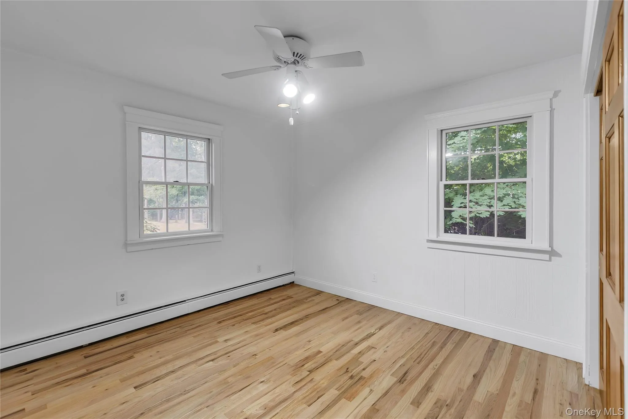 Bright interior bedroom featuring wood-finish flooring, white walls, and a ceiling fan with integrated lighting. Double door closet Bright interior bedroom featuring wood-finish flooring, white walls, and a ceiling fan with integrated lighting. Double door closet