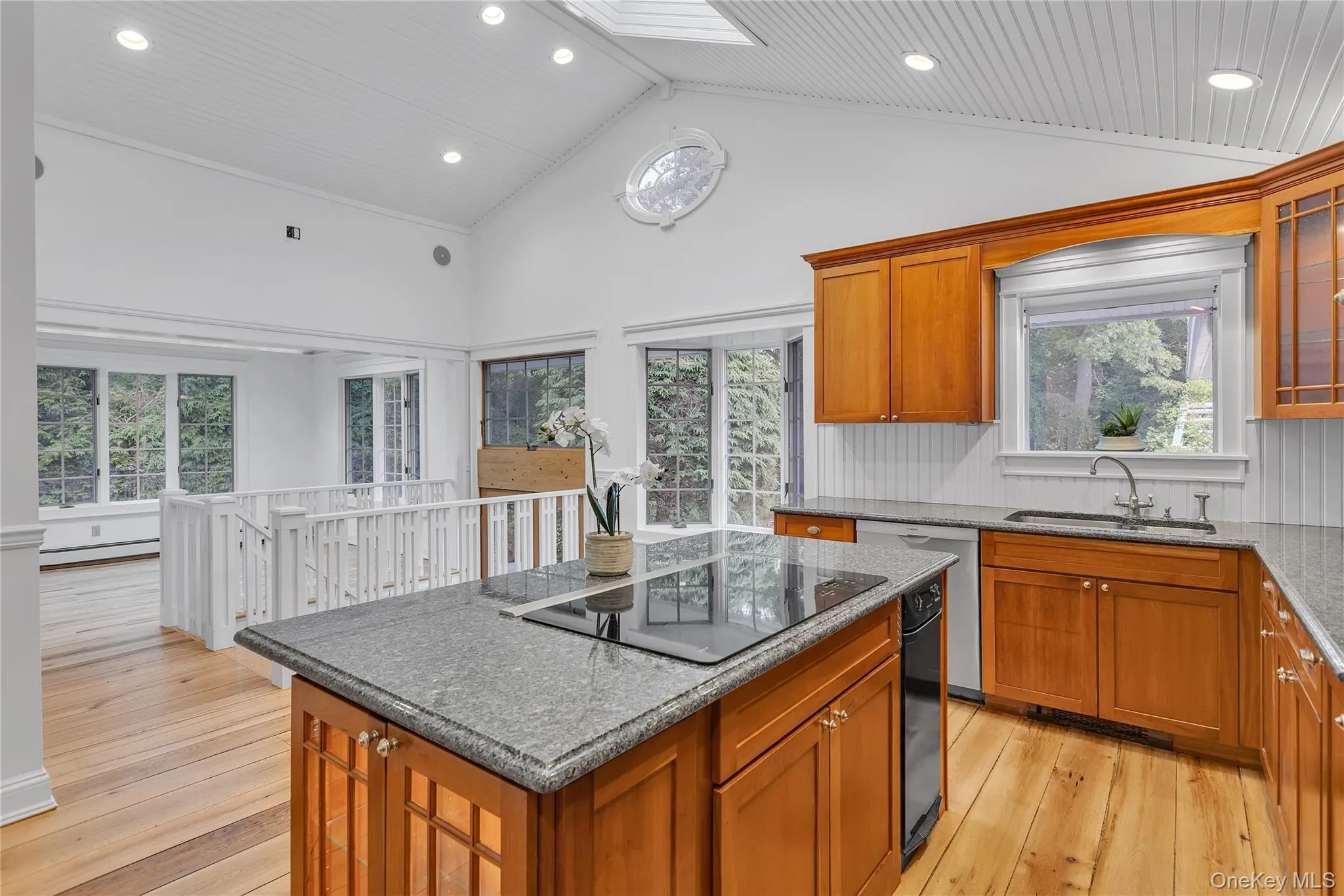 Kitchen featuring a center island with integrated cooktop, granite countertops, wood cabinetry, and wood-finish flooring Kitchen featuring a center island with integrated cooktop, granite countertops, wood cabinetry, and wood-finish flooring