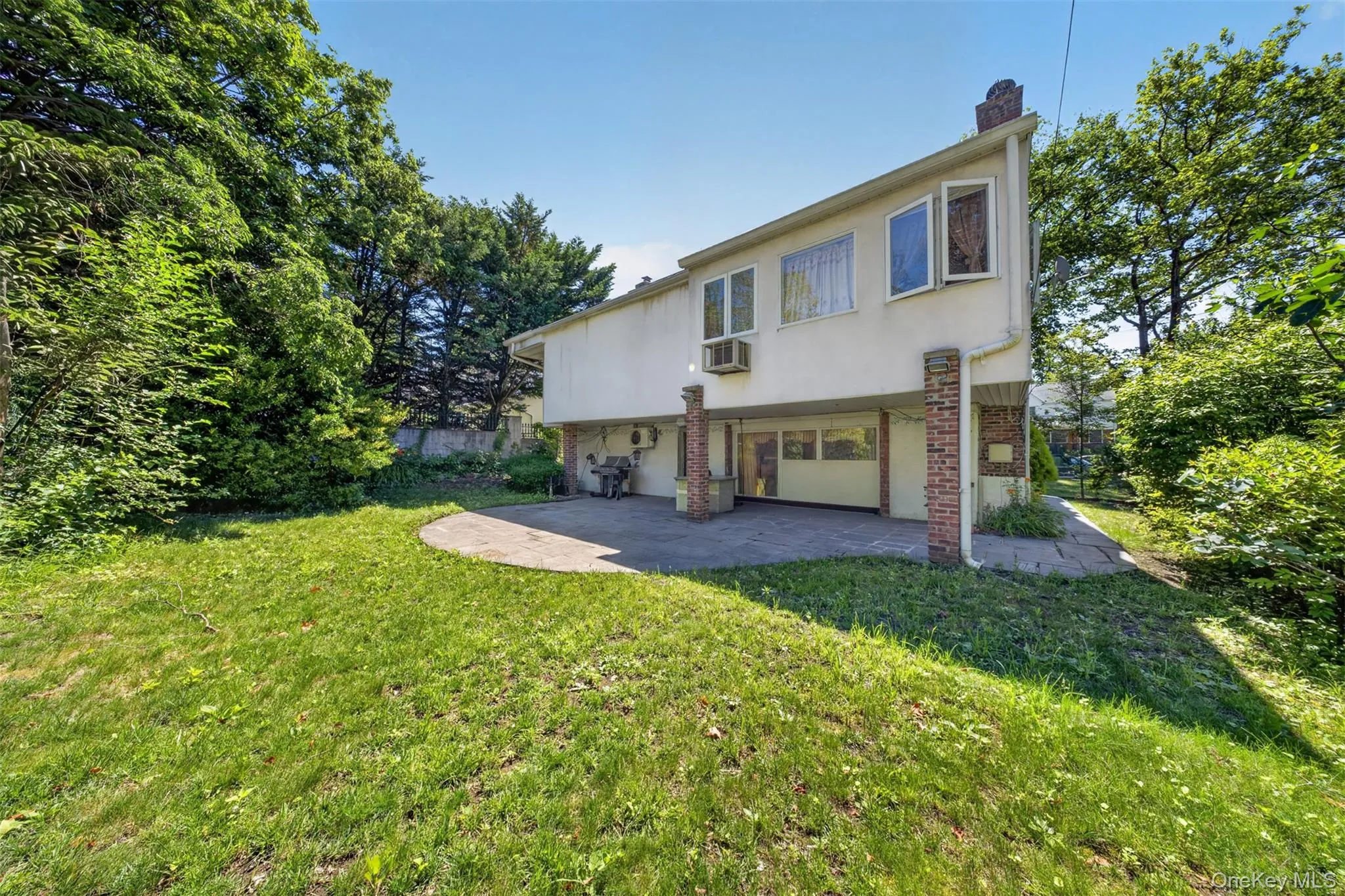 Rear exterior featuring a stucco facade, multiple windows, and a ground-level patio Rear exterior featuring a stucco facade, multiple windows, and a ground-level patio