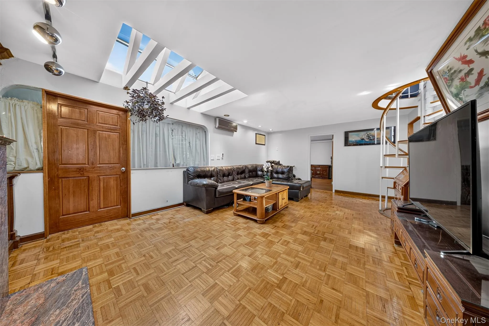 Living area featuring parquet wood-finish flooring, a skylight array, and a spiral staircase with wood treads and white risers Living area featuring parquet wood-finish flooring, a skylight array, and a spiral staircase with wood treads and white risers