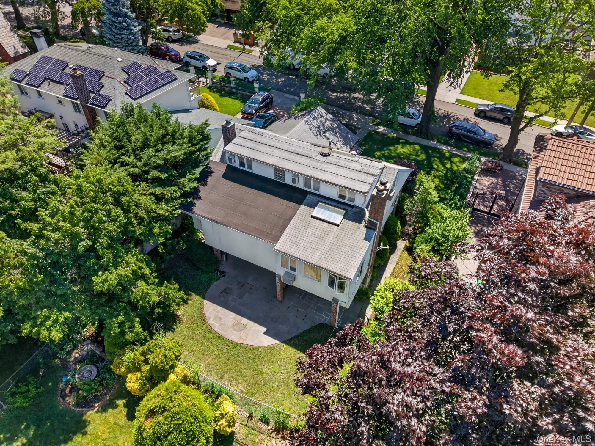 Rear exterior featuring a patio, green lawn, mature trees, and a skylight Rear exterior featuring a patio, green lawn, mature trees, and a skylight