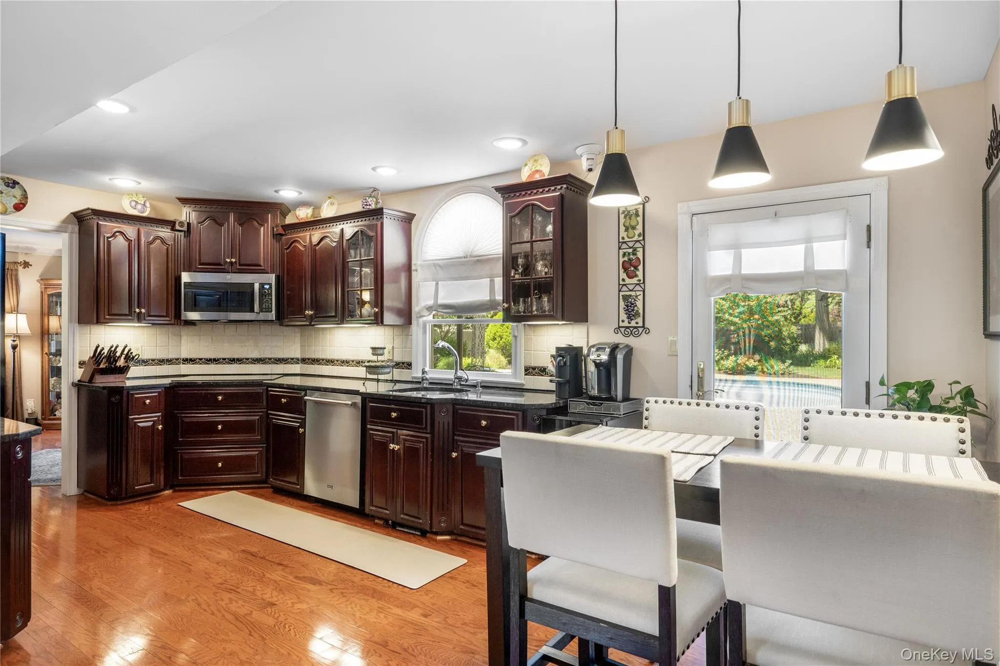 Kitchen featuring wood-finish flooring, dark wood cabinetry, stainless steel appliances, and dark countertops Kitchen featuring wood-finish flooring, dark wood cabinetry, stainless steel appliances, and dark countertops