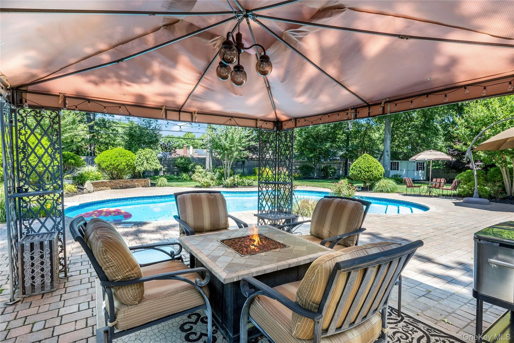Covered outdoor entertaining area featuring a built-in fire pit, paved patio, and in-ground swimming pool Covered outdoor entertaining area featuring a built-in fire pit, paved patio, and in-ground swimming pool