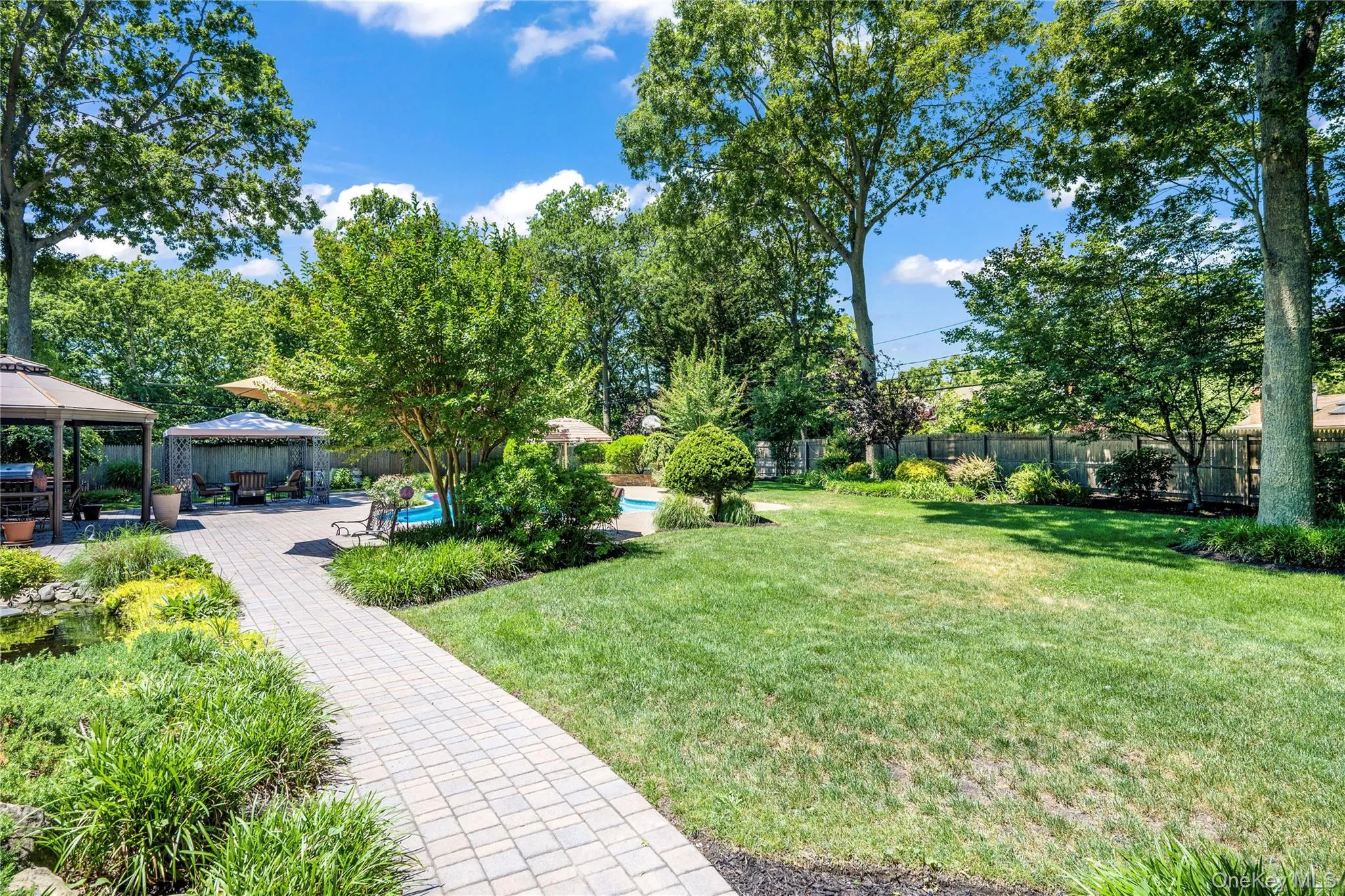Expansive backyard featuring a paver patio with multiple gazebos, a swimming pool, and a pond Expansive backyard featuring a paver patio with multiple gazebos, a swimming pool, and a pond