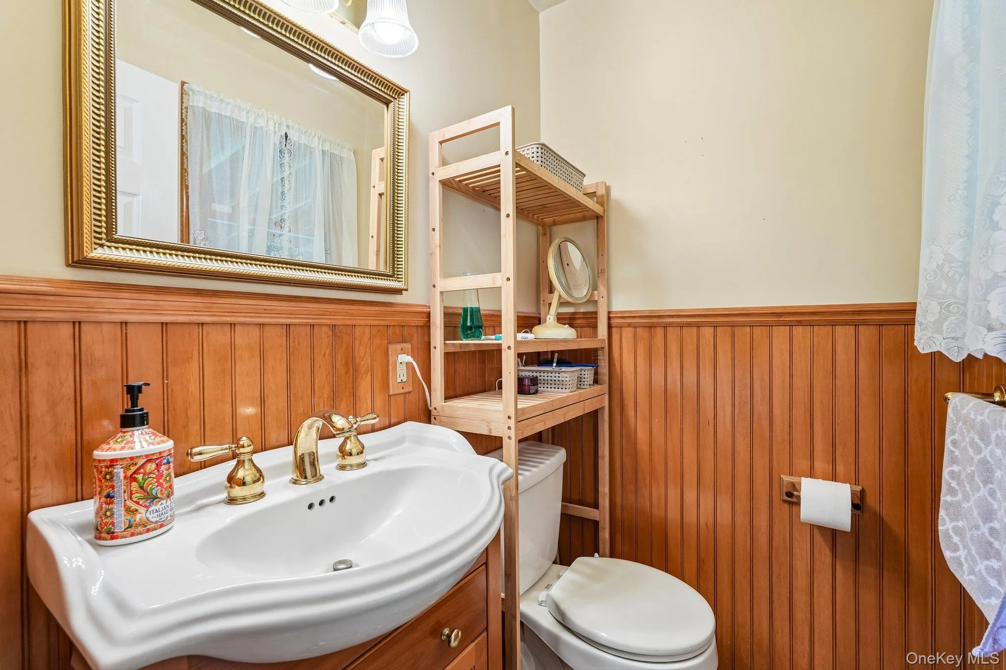 Bathroom with wood paneling, a white ceramic sink, and a vanity with a gold-finish faucet Bathroom with wood paneling, a white ceramic sink, and a vanity with a gold-finish faucet
