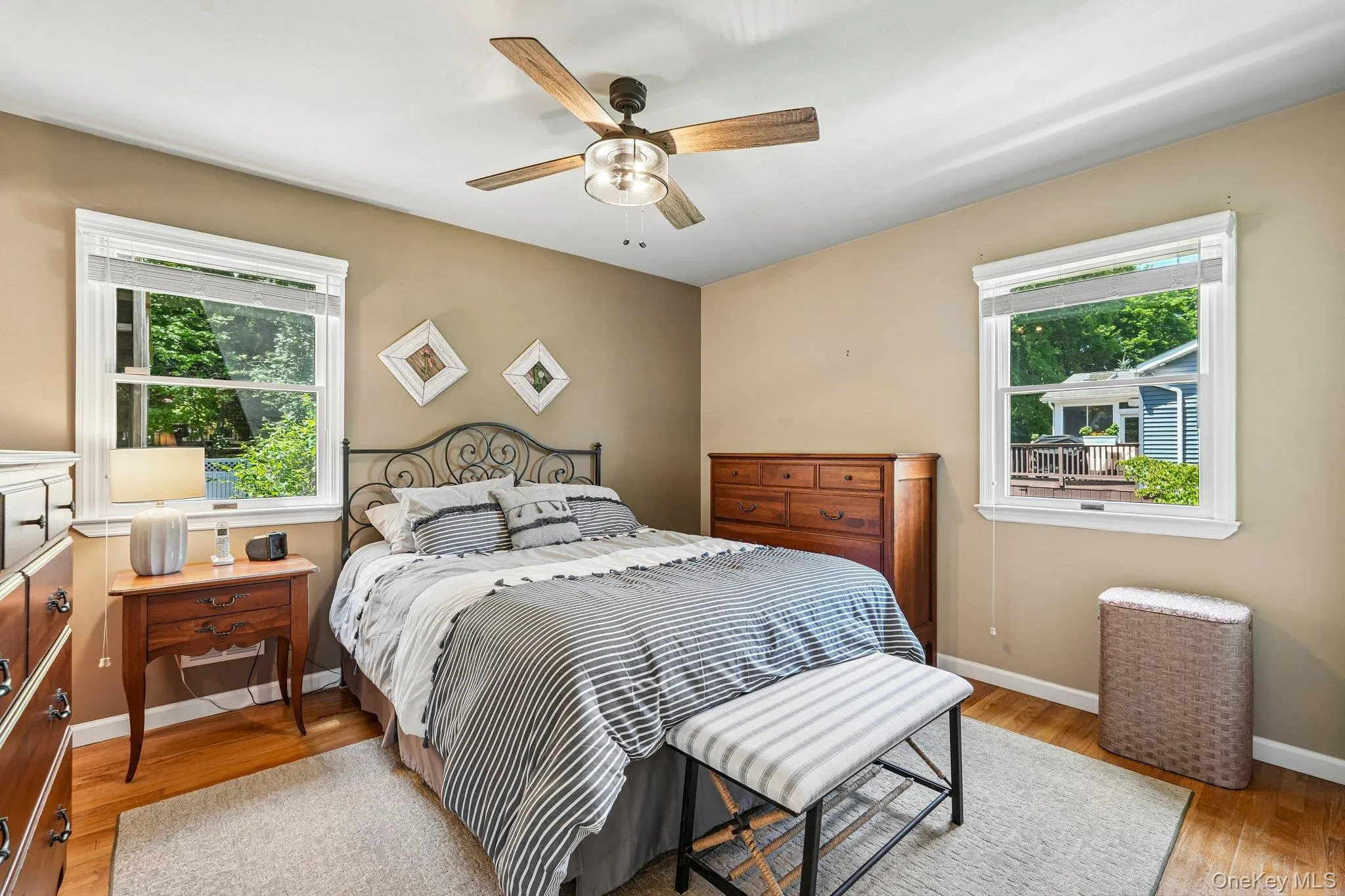 Bedroom featuring two windows with white trim, a ceiling fan with light fixture, light wood-finish flooring, and a neutral wall color Bedroom featuring two windows with white trim, a ceiling fan with light fixture, light wood-finish flooring, and a neutral wall color