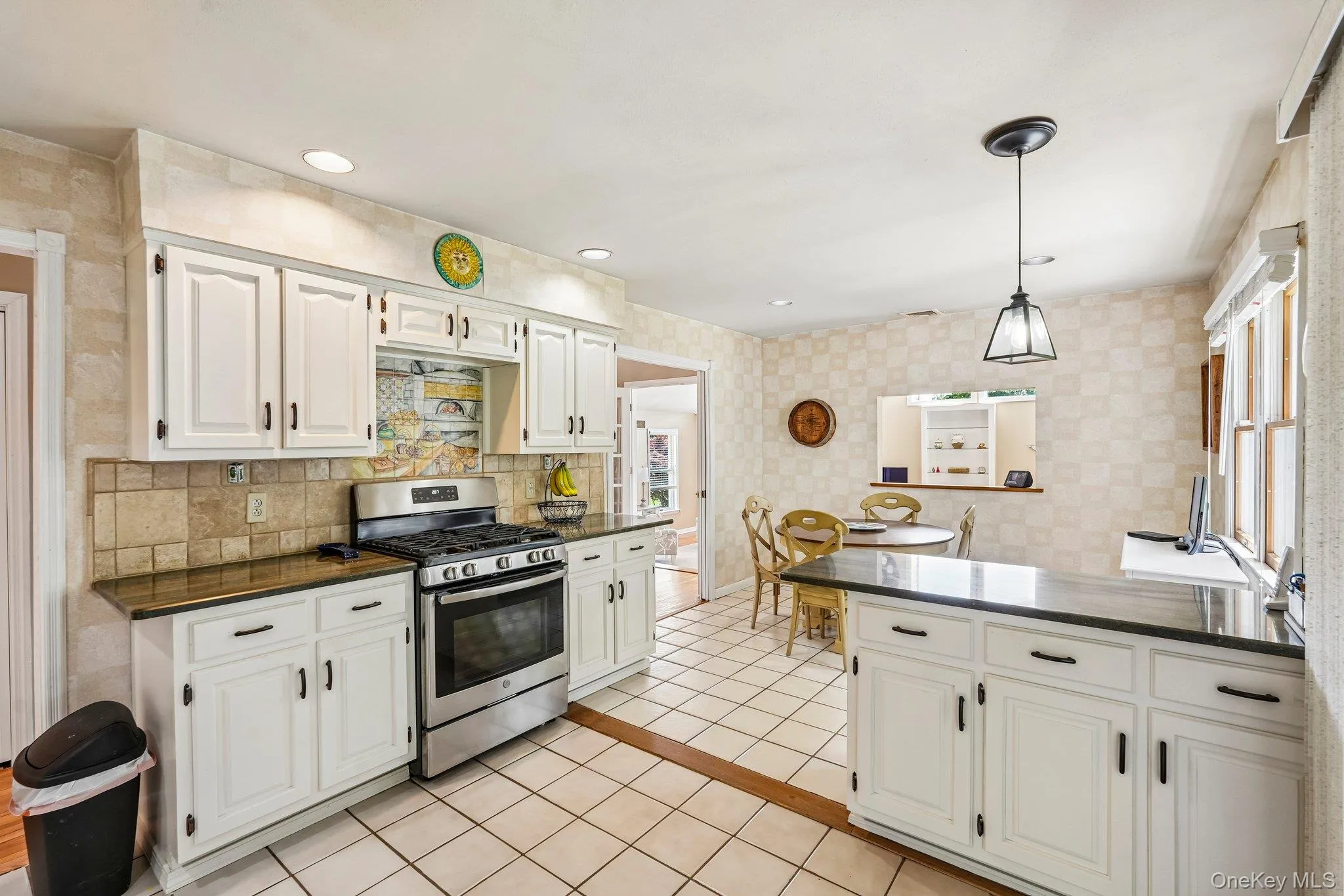Kitchen featuring white cabinetry, dark countertops, a stainless steel gas range, and square tile flooring Kitchen featuring white cabinetry, dark countertops, a stainless steel gas range, and square tile flooring