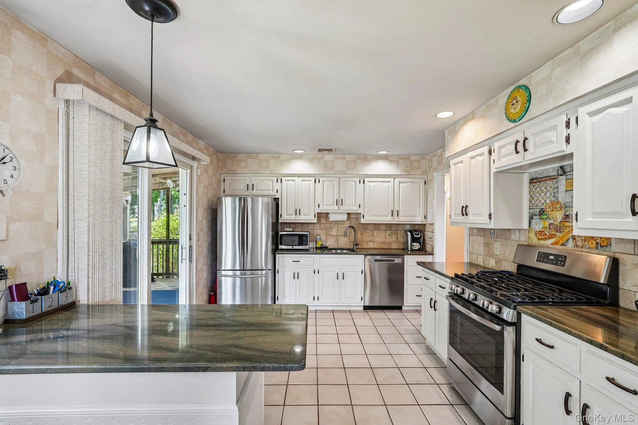Kitchen featuring white cabinetry, stainless steel appliances, dark stone countertops, a tile backsplash, and tile flooring Kitchen featuring white cabinetry, stainless steel appliances, dark stone countertops, a tile backsplash, and tile flooring