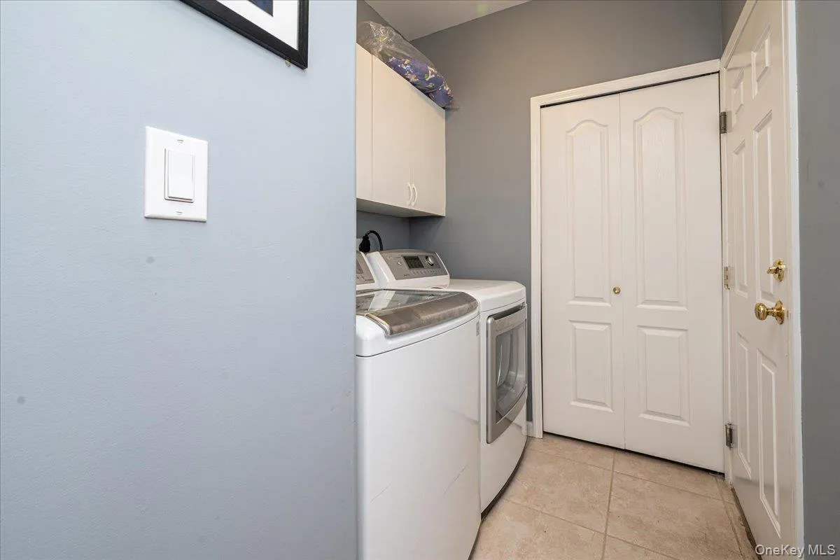 Dedicated laundry area featuring tile flooring, white cabinetry, and bi-fold closet doors Dedicated laundry area featuring tile flooring, white cabinetry, and bi-fold closet doors