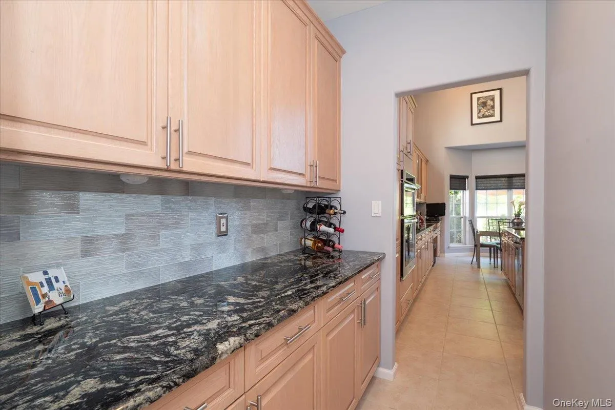 Butlers Pantry featuring light wood-finish cabinetry, dark patterned countertops, a textured Glass tile backsplash, and stainless steel appliances Butlers Pantry featuring light wood-finish cabinetry, dark patterned countertops, a textured Glass tile backsplash, and stainless steel appliances
