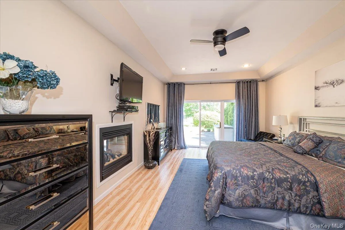 Spacious Primary Bedroom With Tray Ceilings featuring wood-finish flooring, a built-in fireplace, and a ceiling fan Spacious Primary Bedroom With Tray Ceilings featuring wood-finish flooring, a built-in fireplace, and a ceiling fan