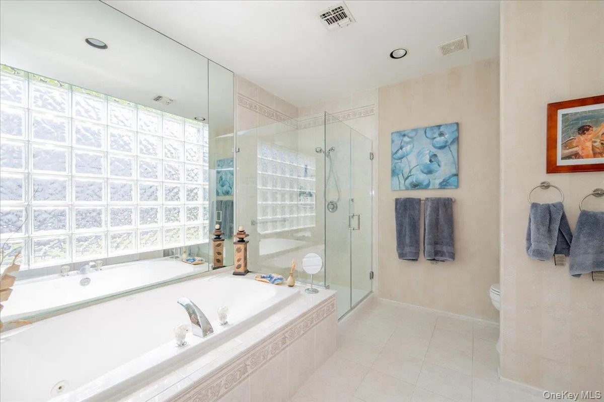 Soaking tub set within a tiled surround, complemented by a glass block window, a glass-enclosed shower, and light-toned floor tile Soaking tub set within a tiled surround, complemented by a glass block window, a glass-enclosed shower, and light-toned floor tile