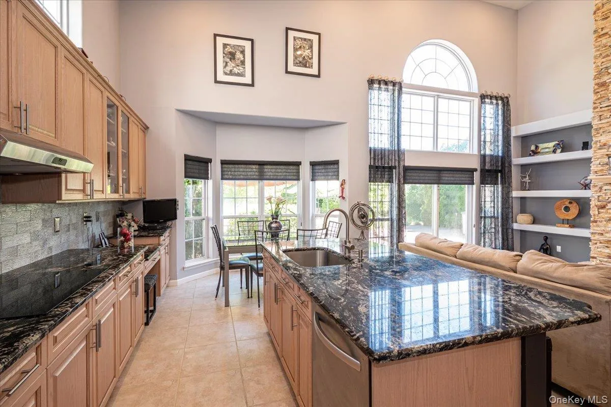 Expansive kitchen featuring a large island with a built-in sink, Granite countertops, light wood cabinetry, and a stone tile backsplash Expansive kitchen featuring a large island with a built-in sink, Granite countertops, light wood cabinetry, and a stone tile backsplash