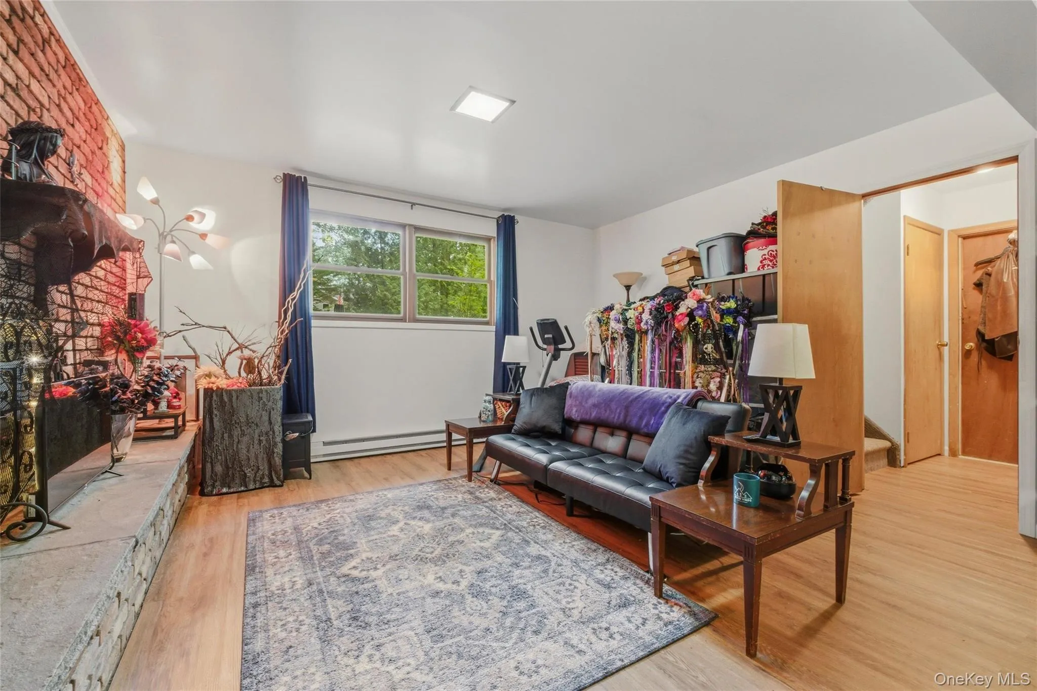 Living space in finished basement featuring wood-finish flooring, a brick accent wall with a stone hearth. Living space in finished basement featuring wood-finish flooring, a brick accent wall with a stone hearth.
