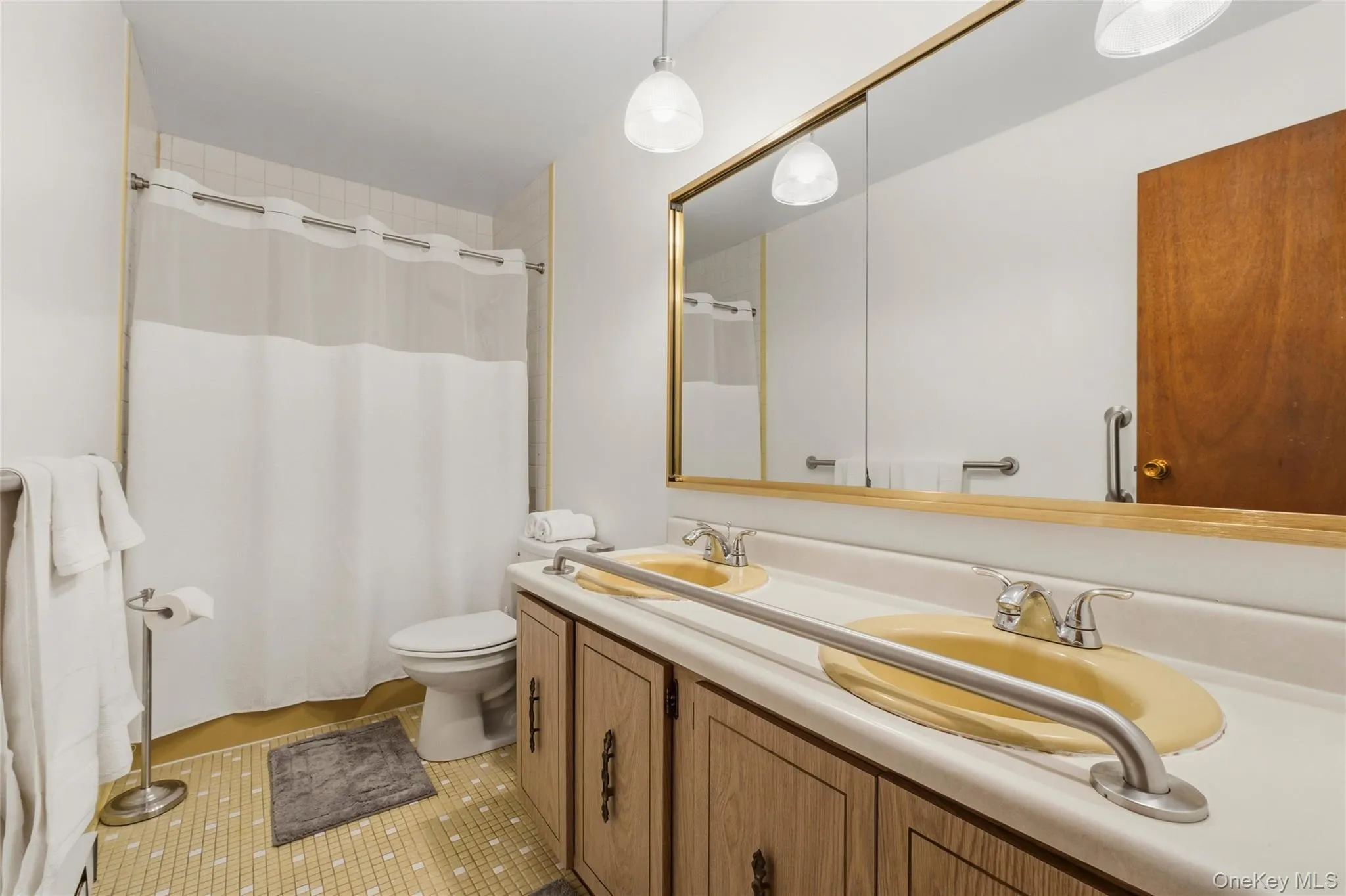 Bathroom featuring a dual vanity with integrated sinks, a full-width mirror, and overhead pendant lighting. Bathroom featuring a dual vanity with integrated sinks, a full-width mirror, and overhead pendant lighting.