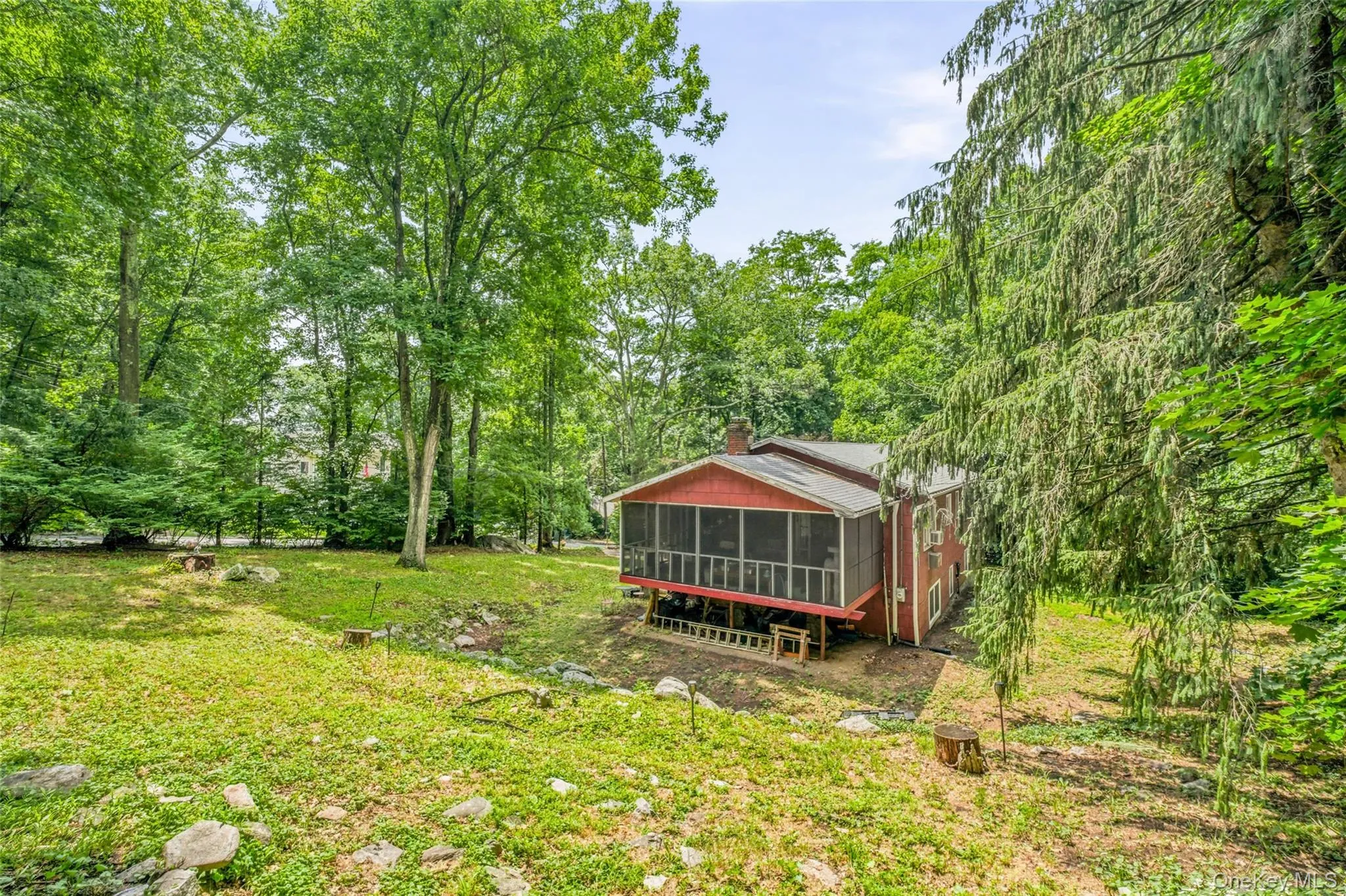 Wooded lot with a red raised ranch dwelling featuring a screened-in porch, and mature wooded lot Wooded lot with a red raised ranch dwelling featuring a screened-in porch, and mature wooded lot
