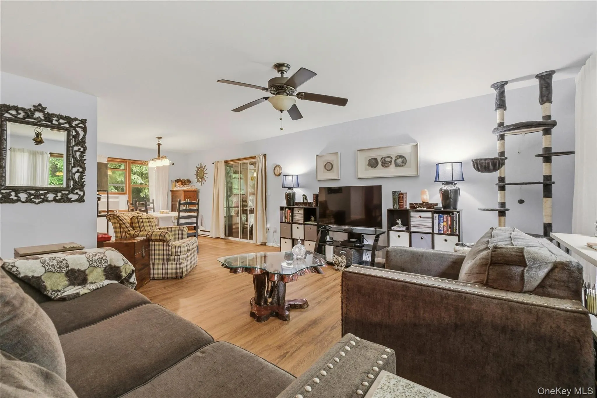 Spacious living area featuring wood-finish flooring, a ceiling fan, and white walls leading to a dining area Spacious living area featuring wood-finish flooring, a ceiling fan, and white walls leading to a dining area
