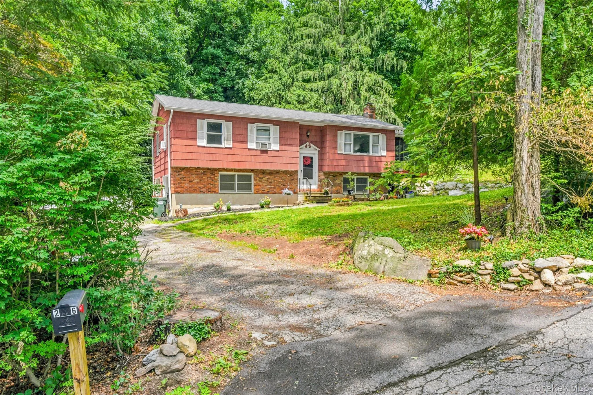 Raised ranch house featuring a red siding and brick facade, a screened-in porch, a paved driveway, and mature landscaping Raised ranch house featuring a red siding and brick facade, a screened-in porch, a paved driveway, and mature landscaping