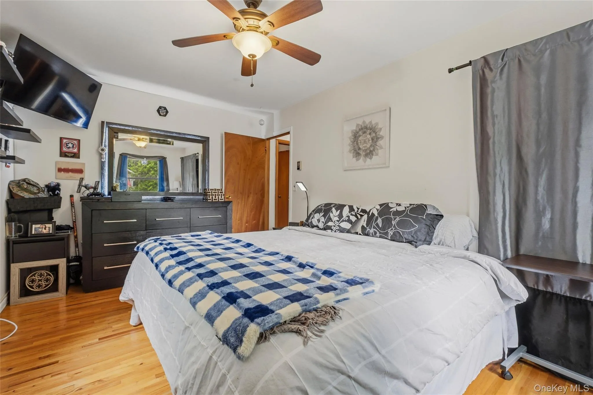 Bright bedroom featuring hardwood flooring, a ceiling fan with integrated lighting, and multiple windows Bright bedroom featuring hardwood flooring, a ceiling fan with integrated lighting, and multiple windows