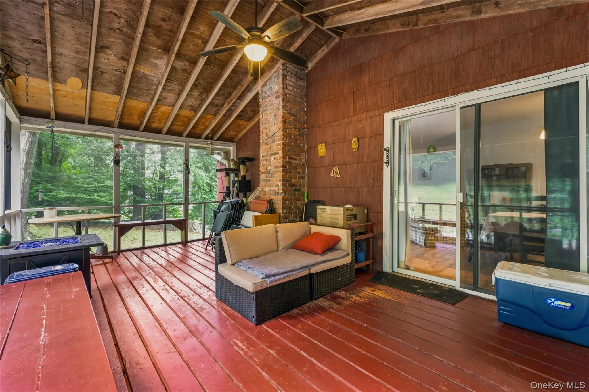 Screened porch with exposed wood beam ceiling, red wood-finish flooring, and a brick-finish column with access to living area Screened porch with exposed wood beam ceiling, red wood-finish flooring, and a brick-finish column with access to living area