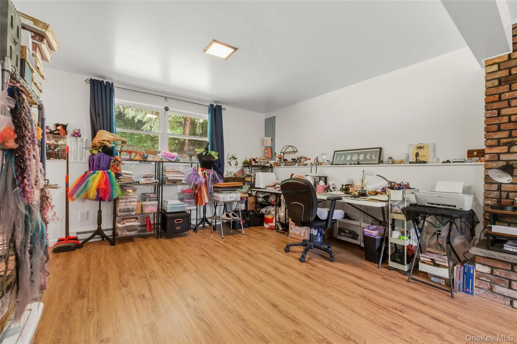 Spacious finished basement space with wood-finish flooring, white walls, and a brick fireplace Spacious finished basement space with wood-finish flooring, white walls, and a brick fireplace