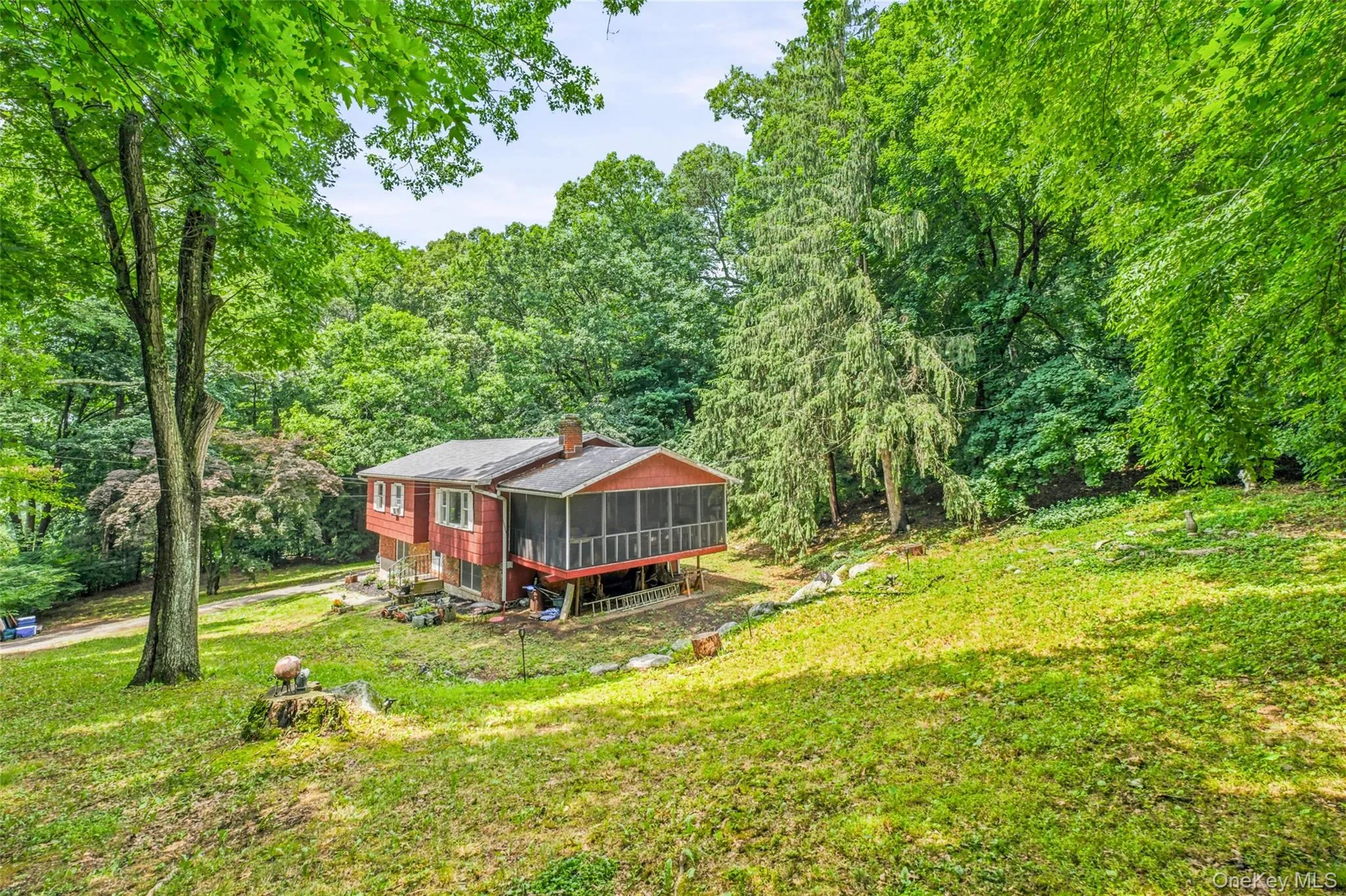 Wooded lot with a red raised ranch dwelling featuring a screened-in porch, and mature wooded lot Wooded lot with a red raised ranch dwelling featuring a screened-in porch, and mature wooded lot