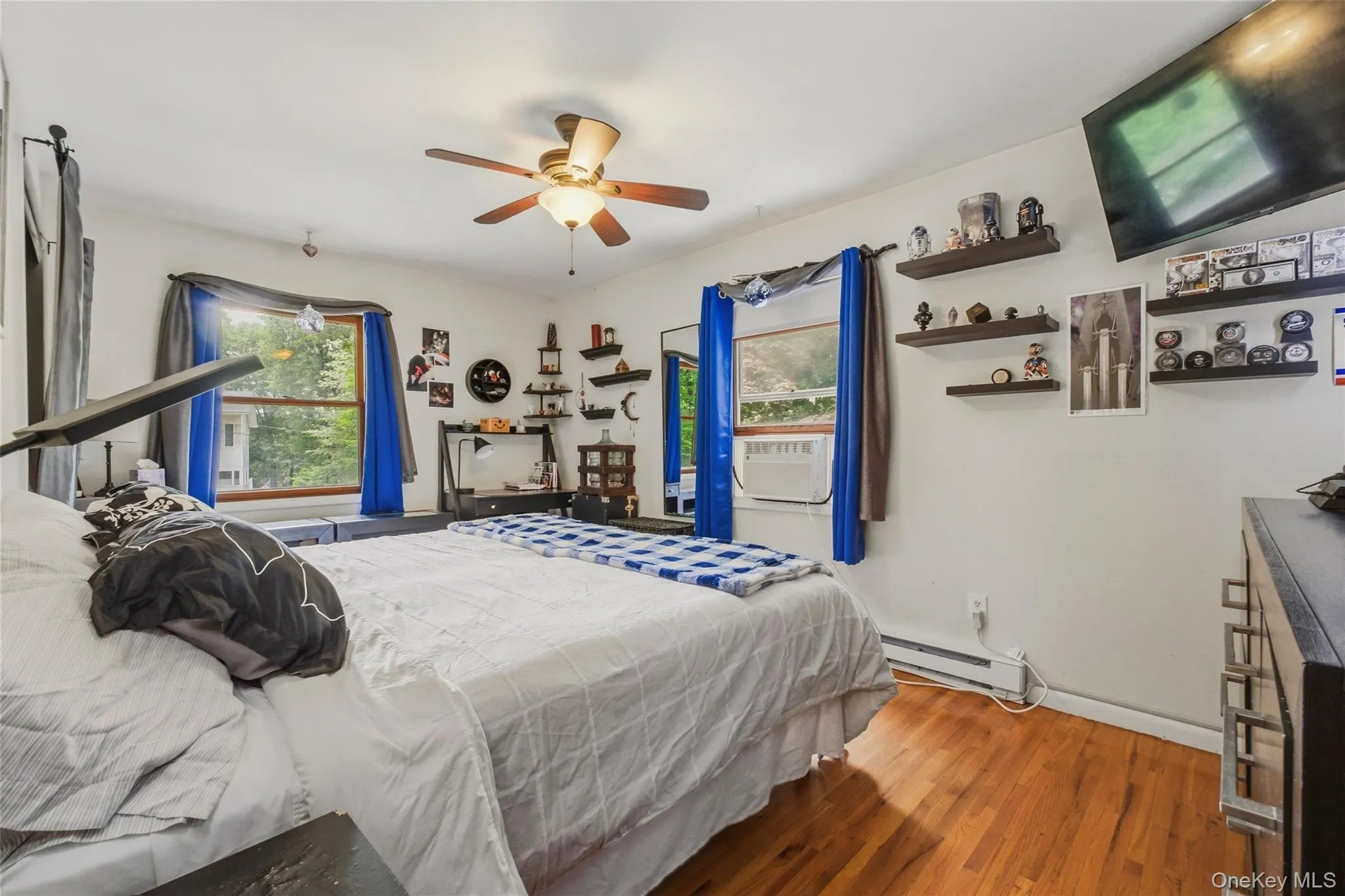 Bright bedroom featuring hardwood flooring, a ceiling fan with integrated lighting, and multiple windows Bright bedroom featuring hardwood flooring, a ceiling fan with integrated lighting, and multiple windows