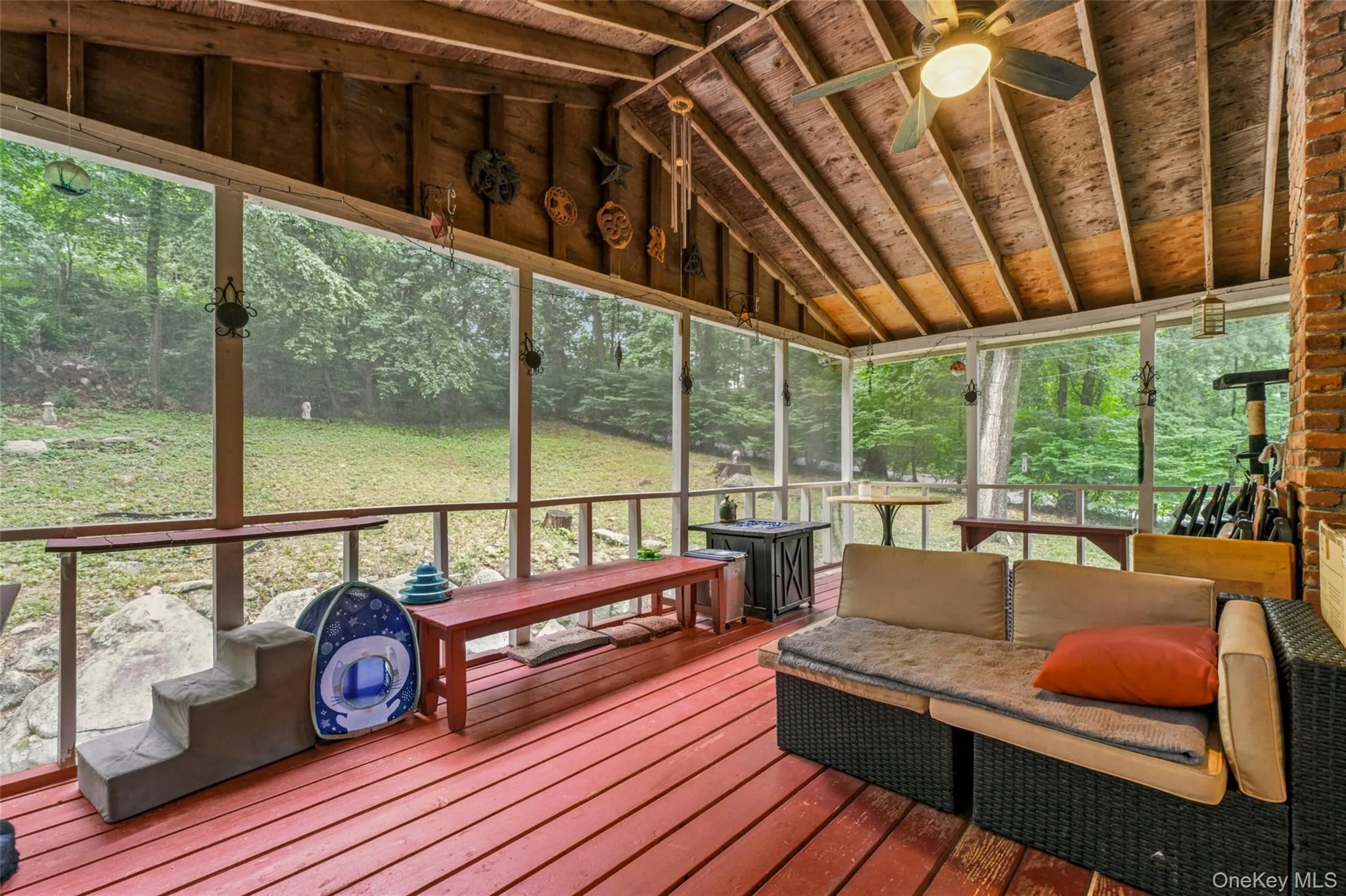 Screened porch with exposed wood beam ceiling, red wood-finish flooring, and a brick-finish column with access to living area Screened porch with exposed wood beam ceiling, red wood-finish flooring, and a brick-finish column with access to living area