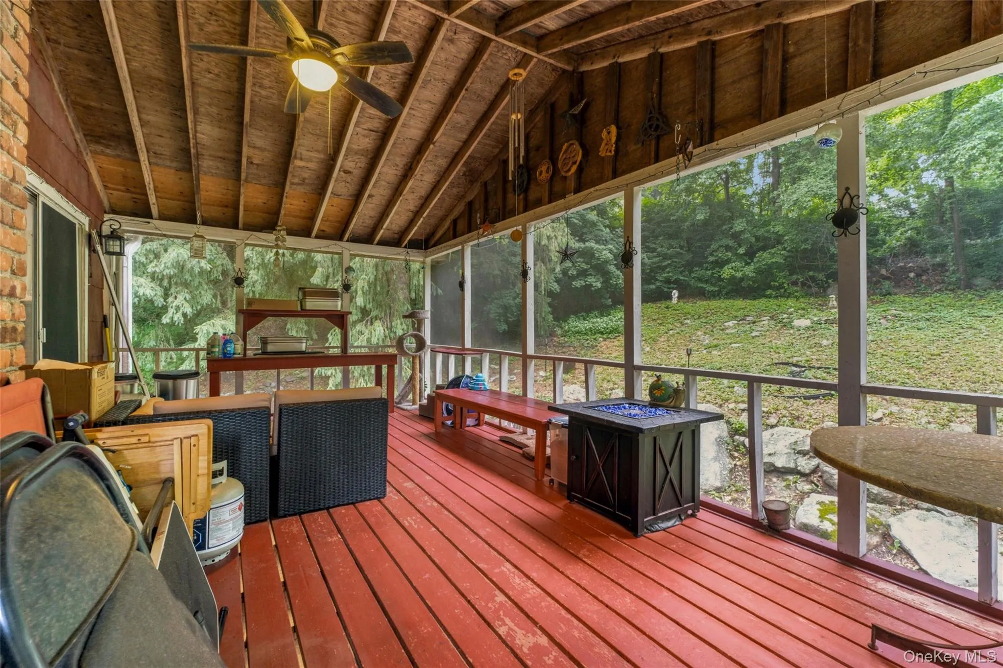 Screened porch with exposed wood beam ceiling, red wood-finish flooring, and a brick-finish column with access to living area Screened porch with exposed wood beam ceiling, red wood-finish flooring, and a brick-finish column with access to living area