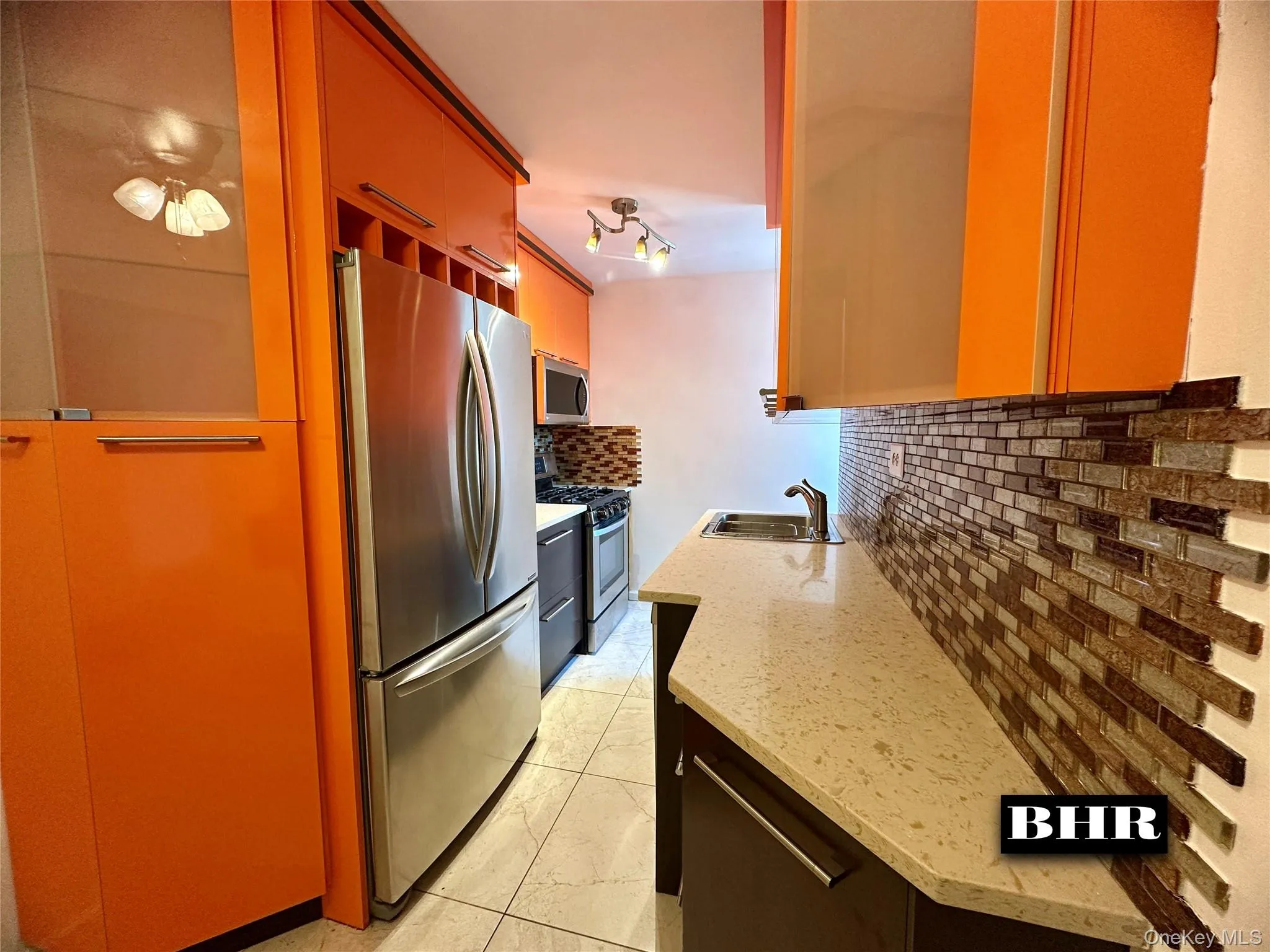 Kitchen with appliances with stainless steel finishes, decorative backsplash, light stone counters, and light tile patterned floors Kitchen with appliances with stainless steel finishes, decorative backsplash, light stone counters, and light tile patterned floors