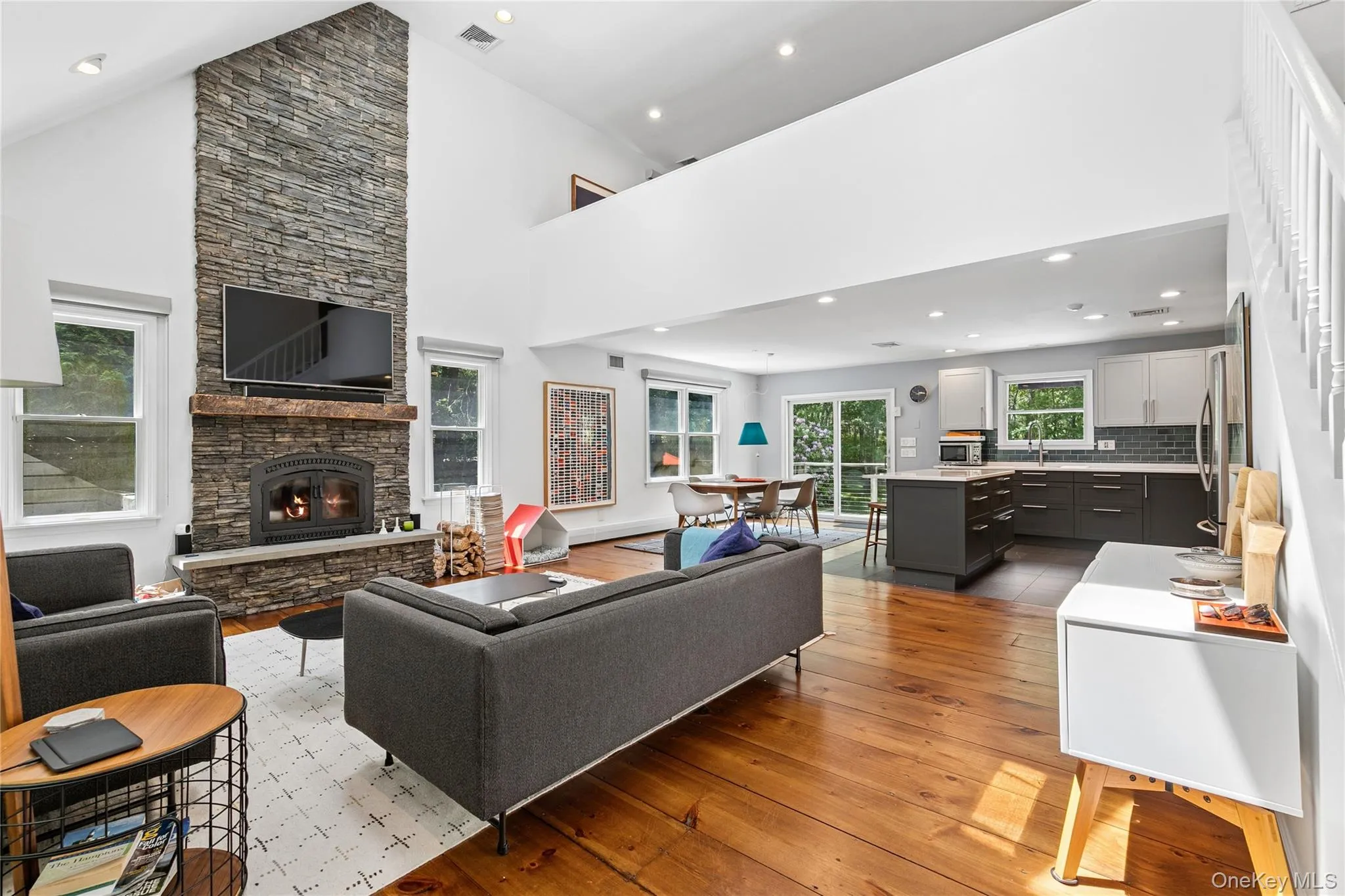 Vaulted ceiling great room featuring a floor-to-ceiling stone fireplace, wood-finish flooring, and a mezzanine overlook Vaulted ceiling great room featuring a floor-to-ceiling stone fireplace, wood-finish flooring, and a mezzanine overlook