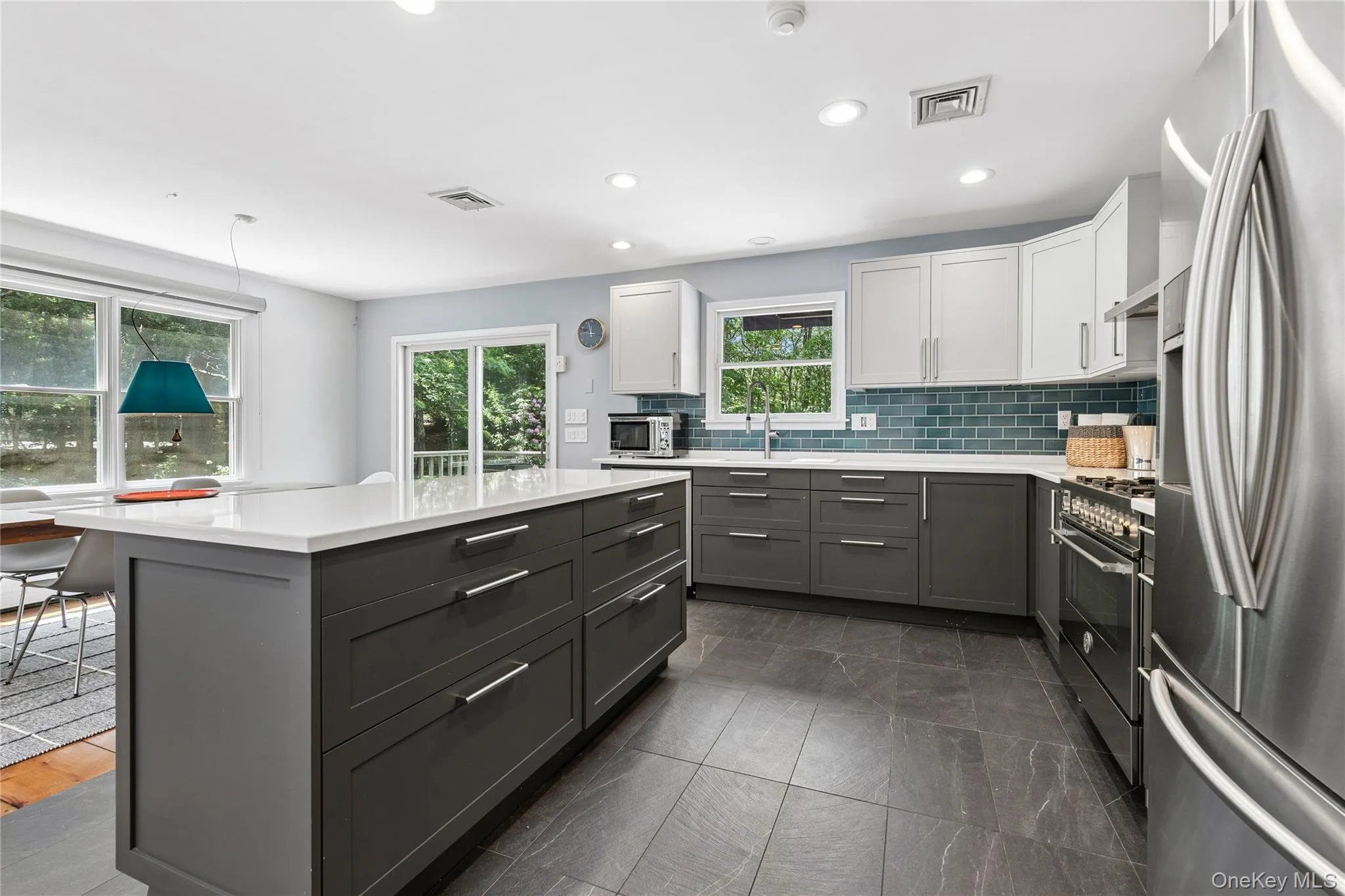 Kitchen featuring a central island with white countertop, stainless steel appliances, dark gray lower cabinetry, and light gray upper cabinetry Kitchen featuring a central island with white countertop, stainless steel appliances, dark gray lower cabinetry, and light gray upper cabinetry